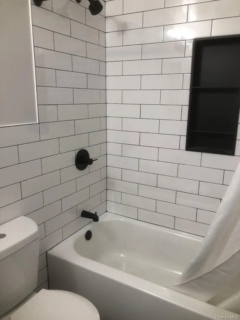 Bathroom featuring white subway tile surround with dark grout, built-in black shower niche, matte black shower fixtures, and a white bathtub Bathroom featuring white subway tile surround with dark grout, built-in black shower niche, matte black shower fixtures, and a white bathtub