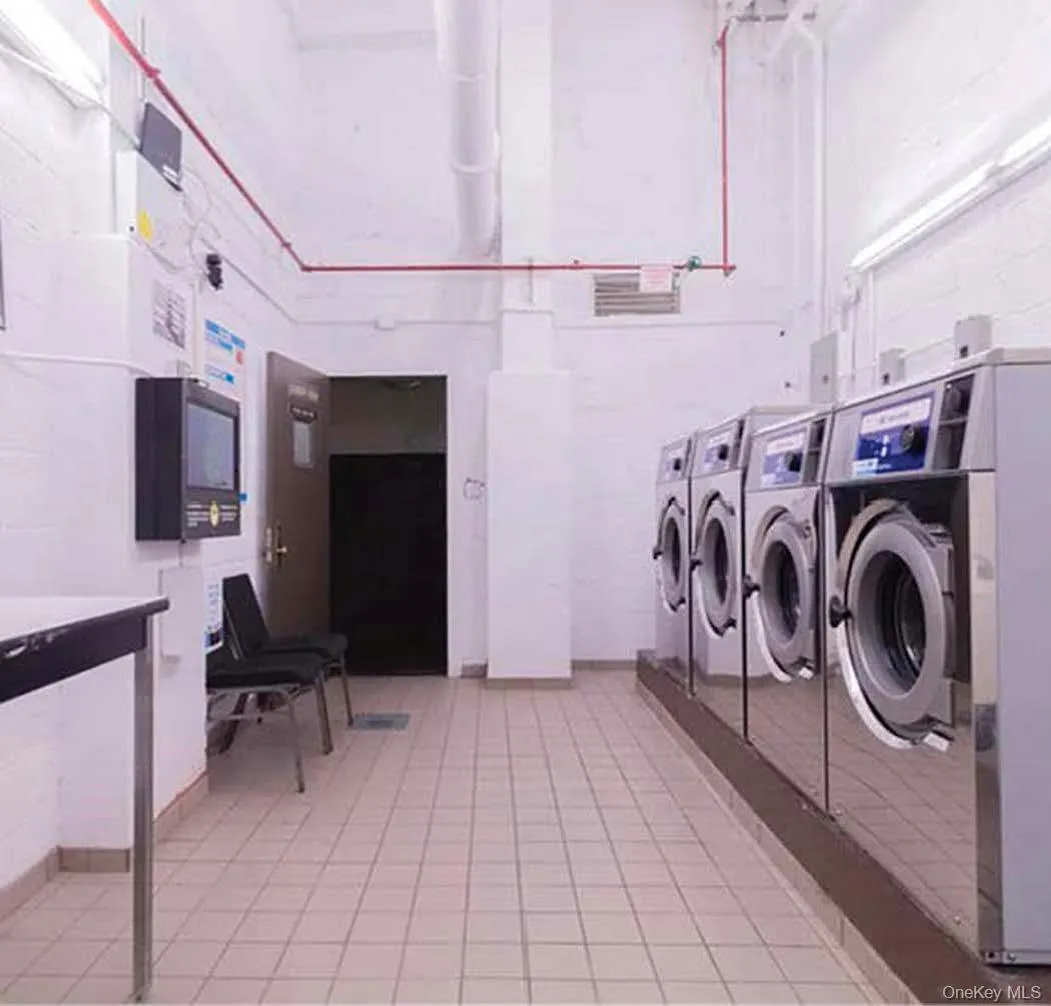 Multiple front-loading washing machines, white tile flooring, and exposed white piping Multiple front-loading washing machines, white tile flooring, and exposed white piping