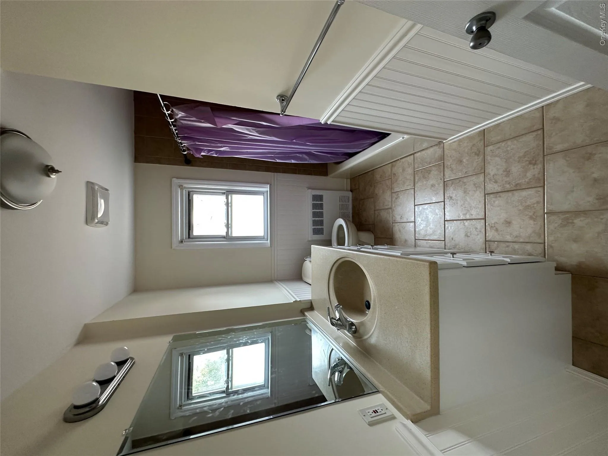 White vanity with integrated sink and chrome faucet, tile flooring, beadboard wainscoting, and a built-in bathtub with shower White vanity with integrated sink and chrome faucet, tile flooring, beadboard wainscoting, and a built-in bathtub with shower