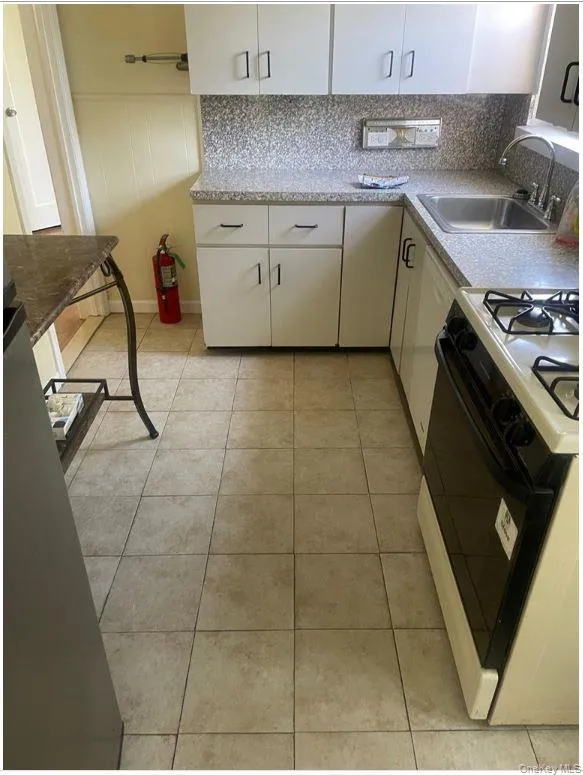 Kitchen featuring stove, decorative backsplash, white cabinetry, and light tile patterned flooring Kitchen featuring stove, decorative backsplash, white cabinetry, and light tile patterned flooring