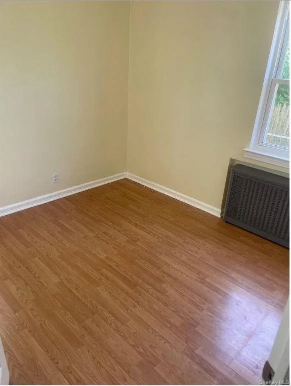 Empty room featuring wood finished floors and radiator heating unit Empty room featuring wood finished floors and radiator heating unit
