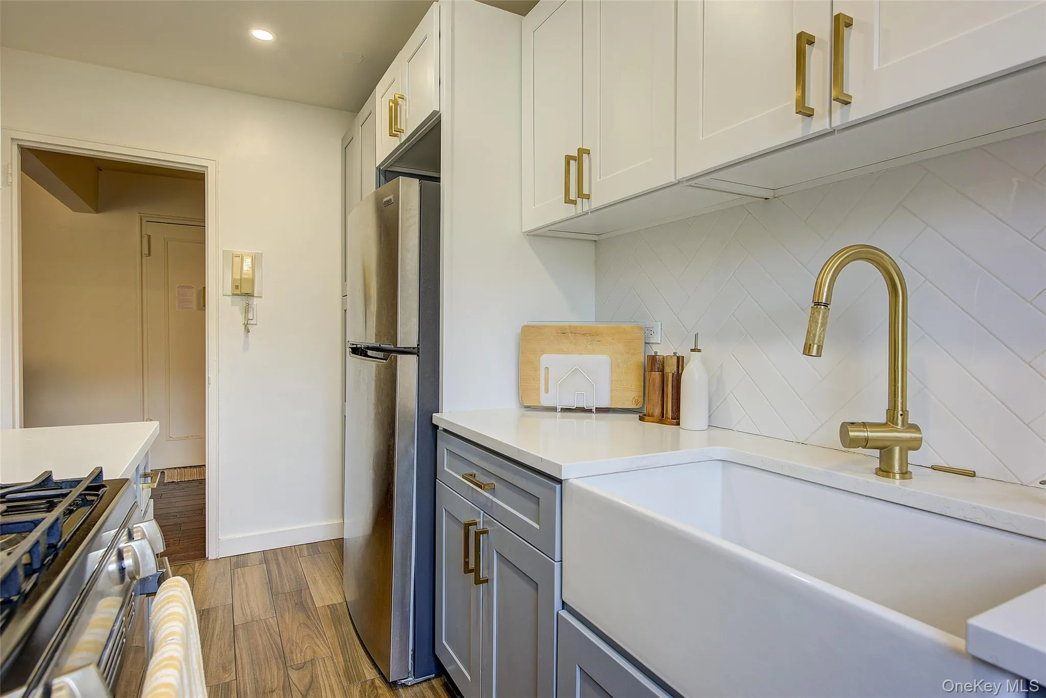 Kitchen with appliances with stainless steel finishes, backsplash, light countertops, dark wood-style floors, and white cabinetry Kitchen with appliances with stainless steel finishes, backsplash, light countertops, dark wood-style floors, and white cabinetry