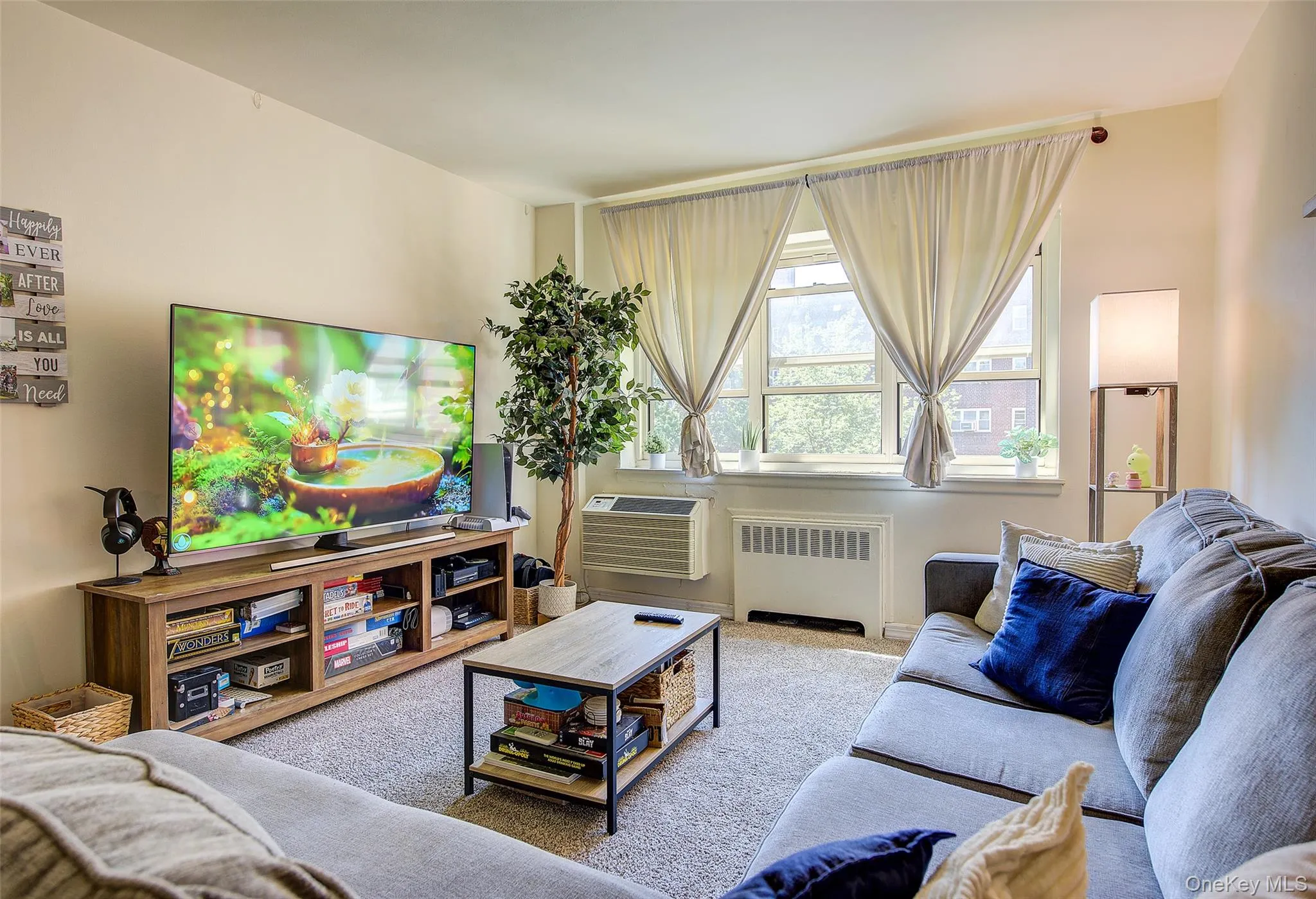 Carpeted living room featuring radiator heating unit and a wall unit AC Carpeted living room featuring radiator heating unit and a wall unit AC