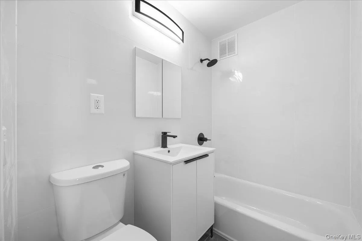 White tiled walls, modern black light fixture, wall-mounted medicine cabinet, white vanity with black hardware, and a white bathtub with a black shower head White tiled walls, modern black light fixture, wall-mounted medicine cabinet, white vanity with black hardware, and a white bathtub with a black shower head