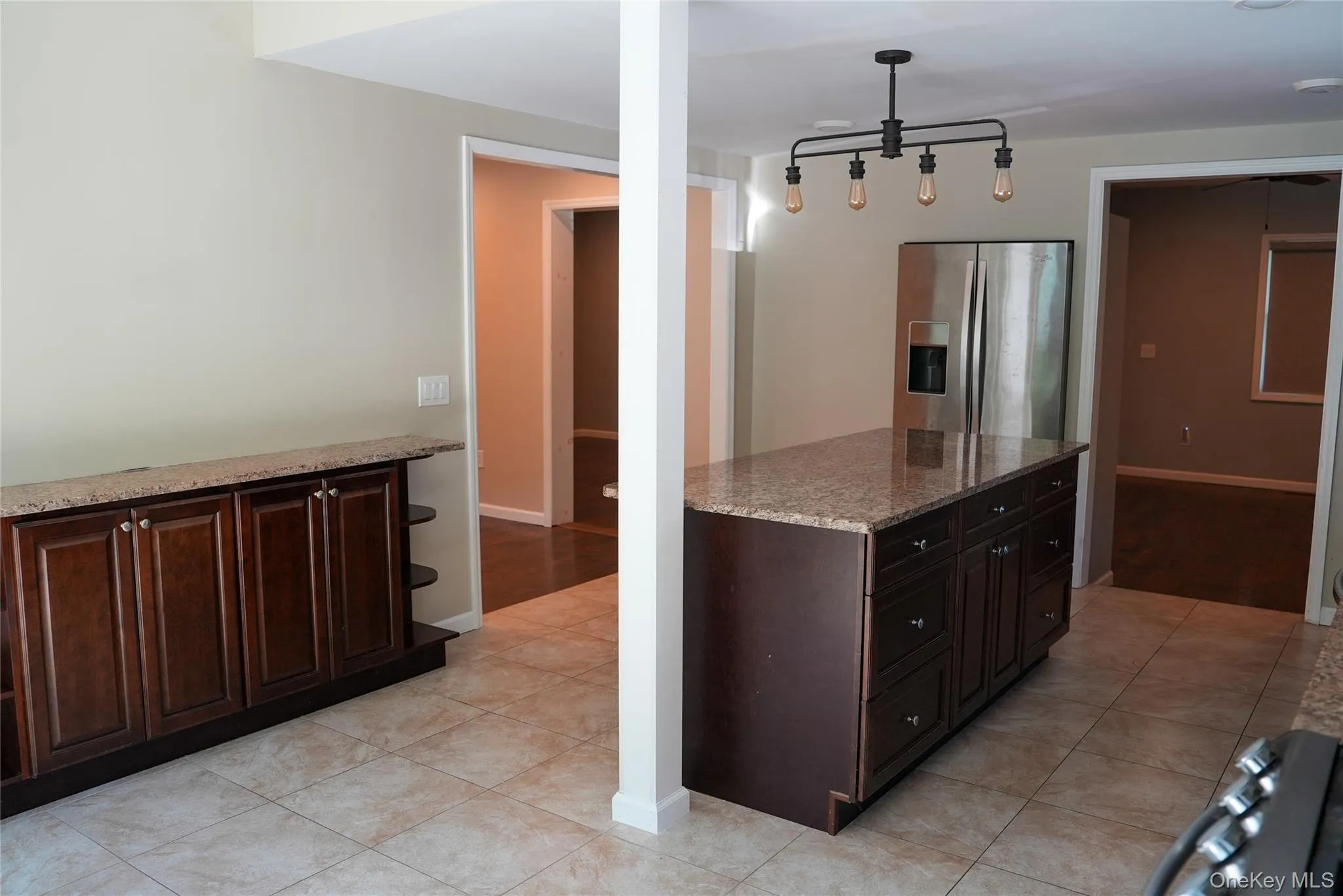 Kitchen featuring a center island with dark wood cabinetry and a light granite-style countertop Kitchen featuring a center island with dark wood cabinetry and a light granite-style countertop