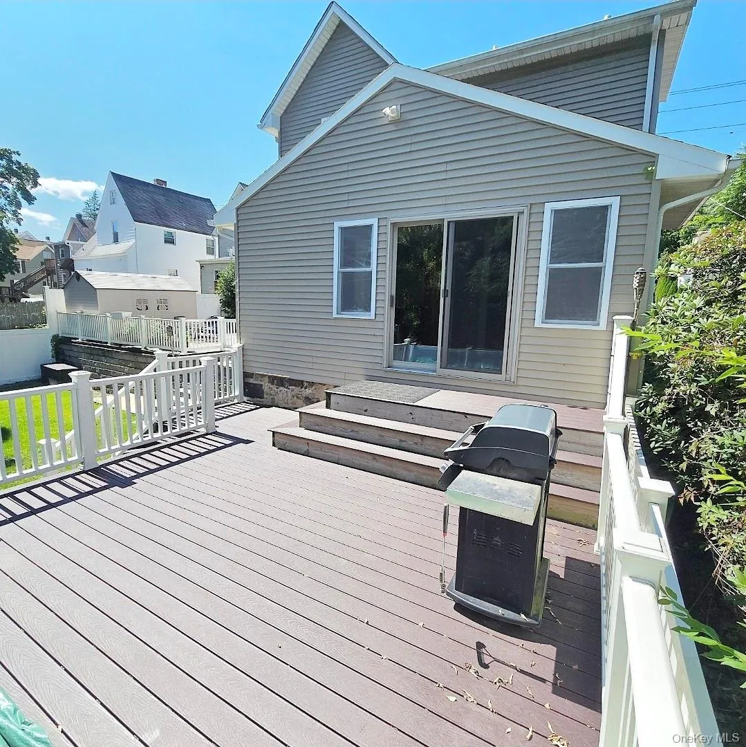 Spacious exterior deck with composite decking and white railing, featuring steps to a sliding glass door entry and two windows Spacious exterior deck with composite decking and white railing, featuring steps to a sliding glass door entry and two windows