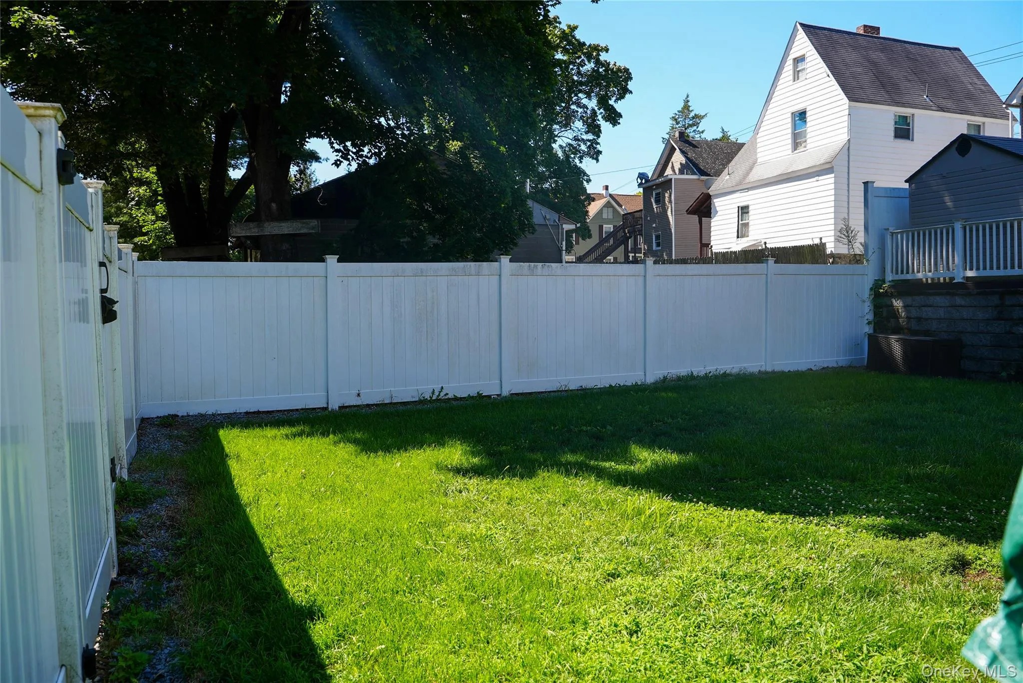 Expansive backyard featuring a manicured lawn, white privacy fencing, and a retaining wall Expansive backyard featuring a manicured lawn, white privacy fencing, and a retaining wall