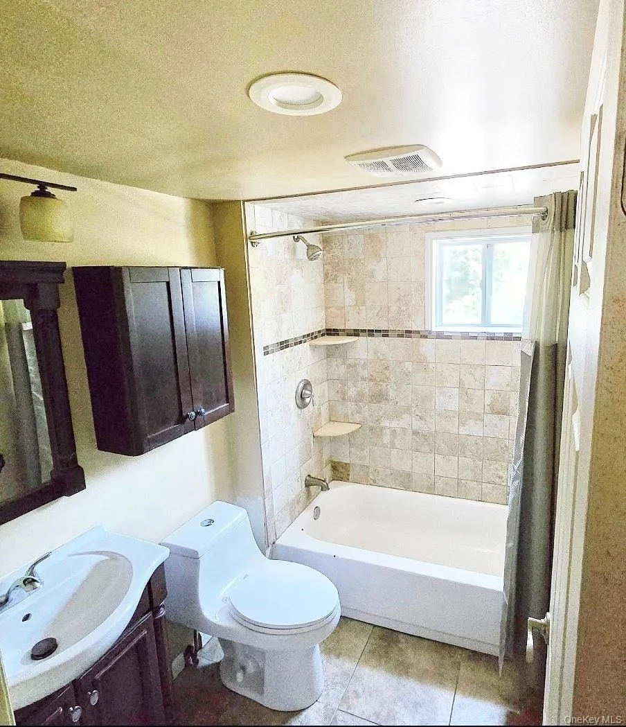 Full bathroom featuring a single vanity, toilet, and a shower-tub combination with tile surround Full bathroom featuring a single vanity, toilet, and a shower-tub combination with tile surround