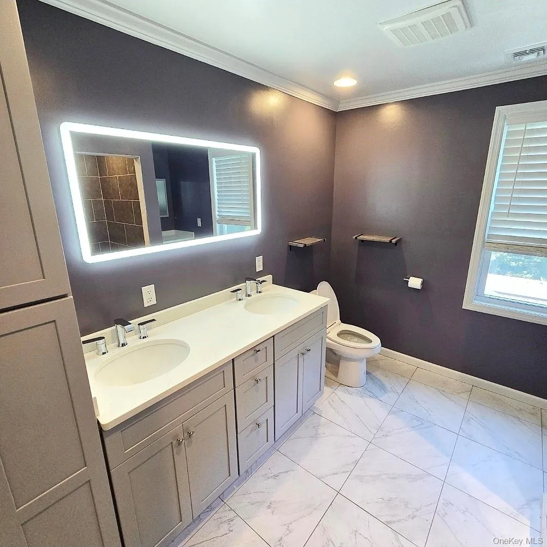 Double vanity with integrated sinks and chrome fixtures, illuminated mirror, and marble-look tile flooring Double vanity with integrated sinks and chrome fixtures, illuminated mirror, and marble-look tile flooring