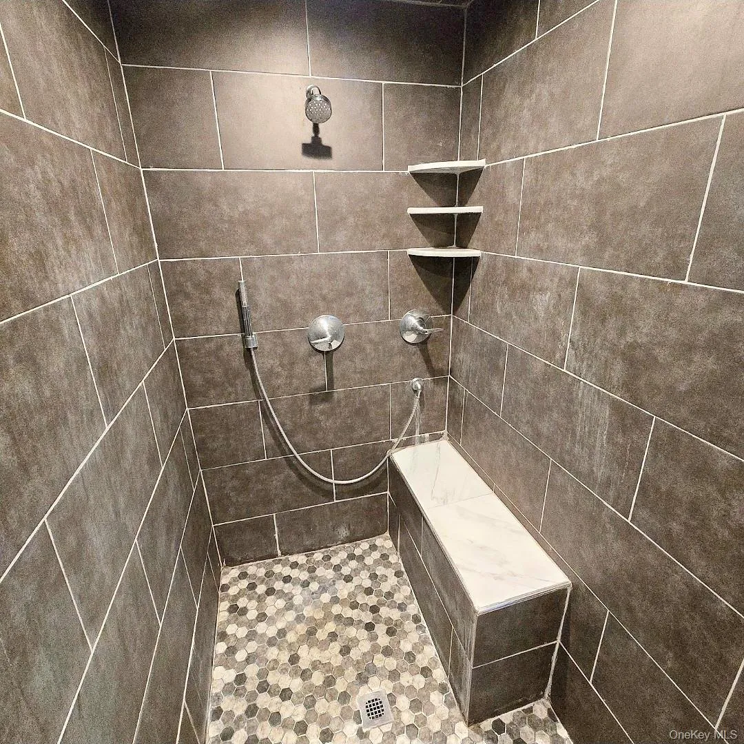 Tiled shower featuring a built-in bench, three corner shelves, a handheld shower head, and a hexagonal floor tile pattern Tiled shower featuring a built-in bench, three corner shelves, a handheld shower head, and a hexagonal floor tile pattern