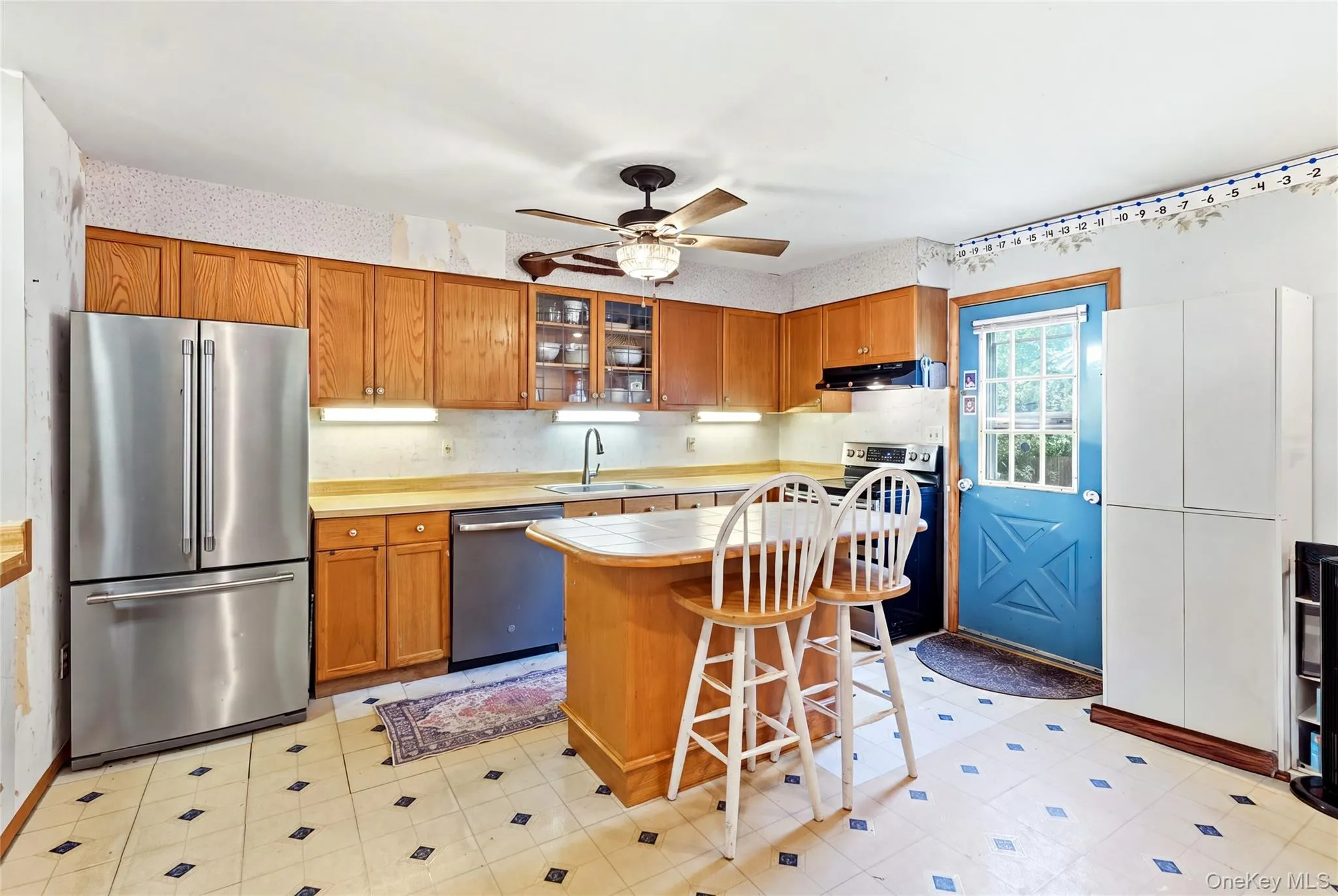 Kitchen featuring wood cabinetry, stainless steel refrigerator and dishwasher, patterned flooring, and a central island Kitchen featuring wood cabinetry, stainless steel refrigerator and dishwasher, patterned flooring, and a central island