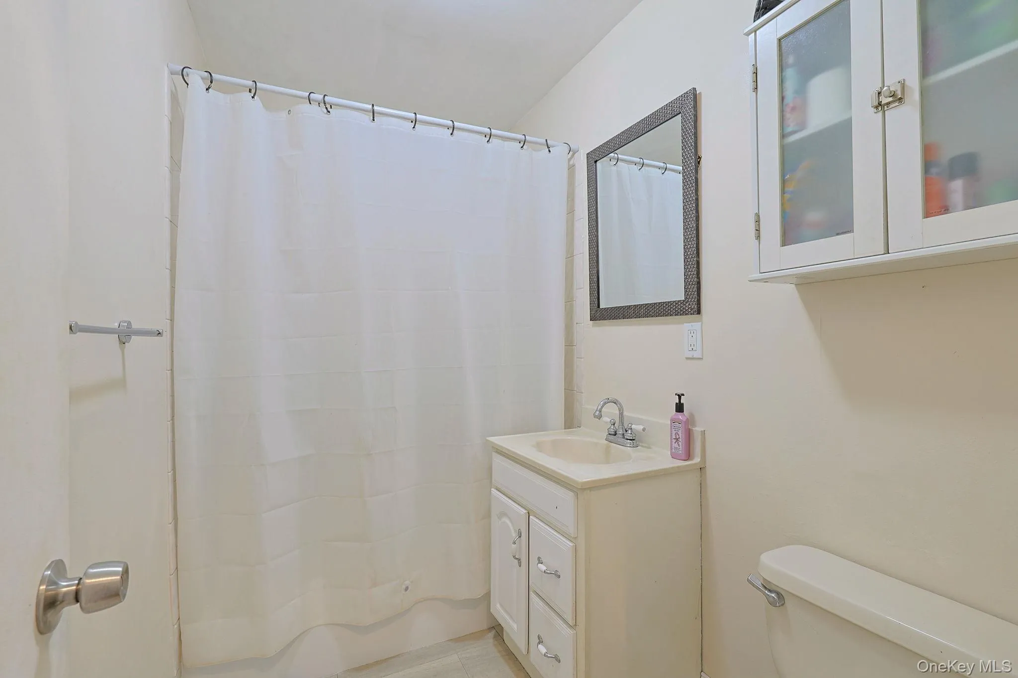 Bathroom featuring a vanity with an integrated sink, wall-mounted mirror, and white cabinetry with frosted glass inserts Bathroom featuring a vanity with an integrated sink, wall-mounted mirror, and white cabinetry with frosted glass inserts