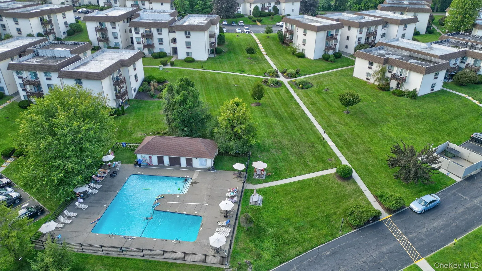 Outdoor swimming pool with surrounding patio, a poolside building, extensive manicured lawns, and paved walkways Outdoor swimming pool with surrounding patio, a poolside building, extensive manicured lawns, and paved walkways