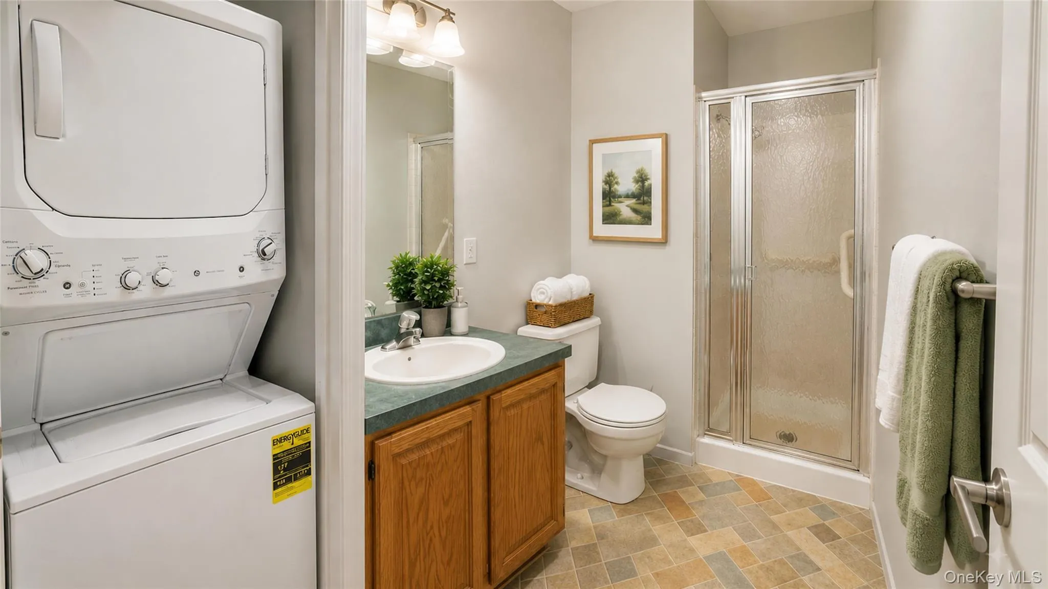 Well-appointed full bath featuring a vanity, tiled flooring, walk-in shower, and conveniently adjacent laundry area. Well-appointed full bath featuring a vanity, tiled flooring, walk-in shower, and conveniently adjacent laundry area.