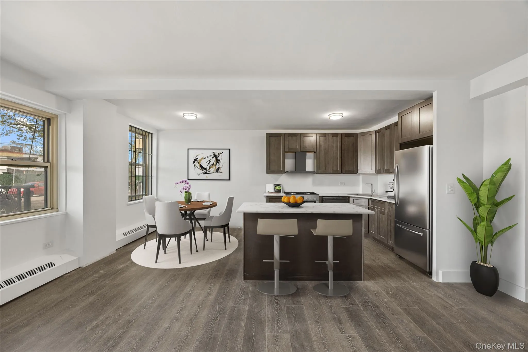 Open-concept living space featuring vinyl flooring, a kitchen with stainless steel appliances, dark wood-finish cabinetry, and a central island with a light-colored countertop Open-concept living space featuring vinyl flooring, a kitchen with stainless steel appliances, dark wood-finish cabinetry, and a central island with a light-colored countertop