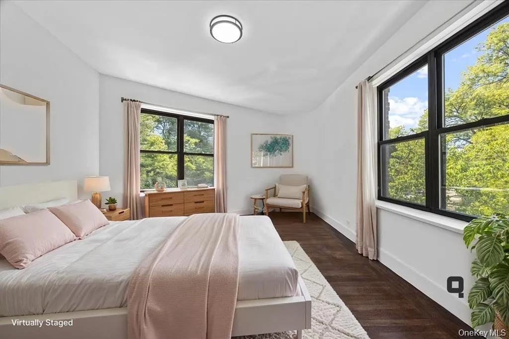 Spacious room featuring dark wood-finish flooring, white walls, two large windows with black frames, and a modern flush-mount ceiling light Spacious room featuring dark wood-finish flooring, white walls, two large windows with black frames, and a modern flush-mount ceiling light