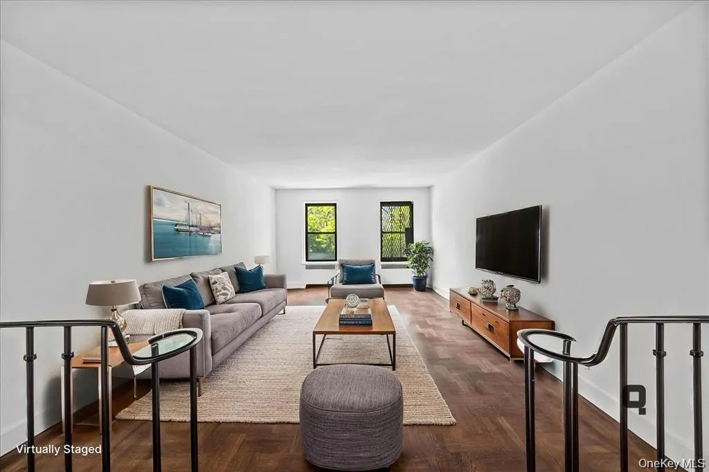Bright living space featuring dark wood-finish flooring, white walls, and a wall-mounted television Bright living space featuring dark wood-finish flooring, white walls, and a wall-mounted television