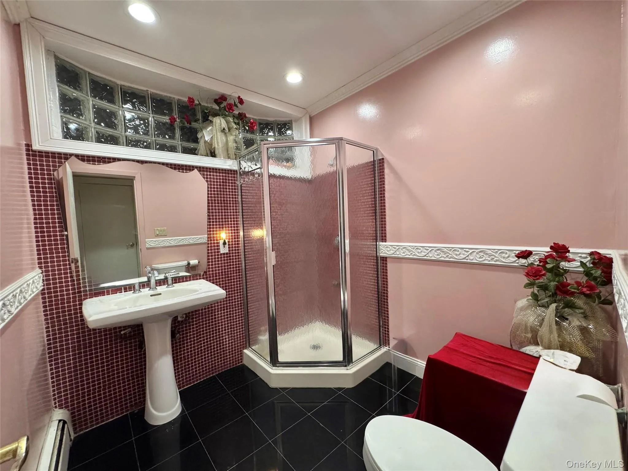 Pedestal sink with chrome fixtures, glass-enclosed shower, black tile flooring, and red mosaic wall tiling Pedestal sink with chrome fixtures, glass-enclosed shower, black tile flooring, and red mosaic wall tiling