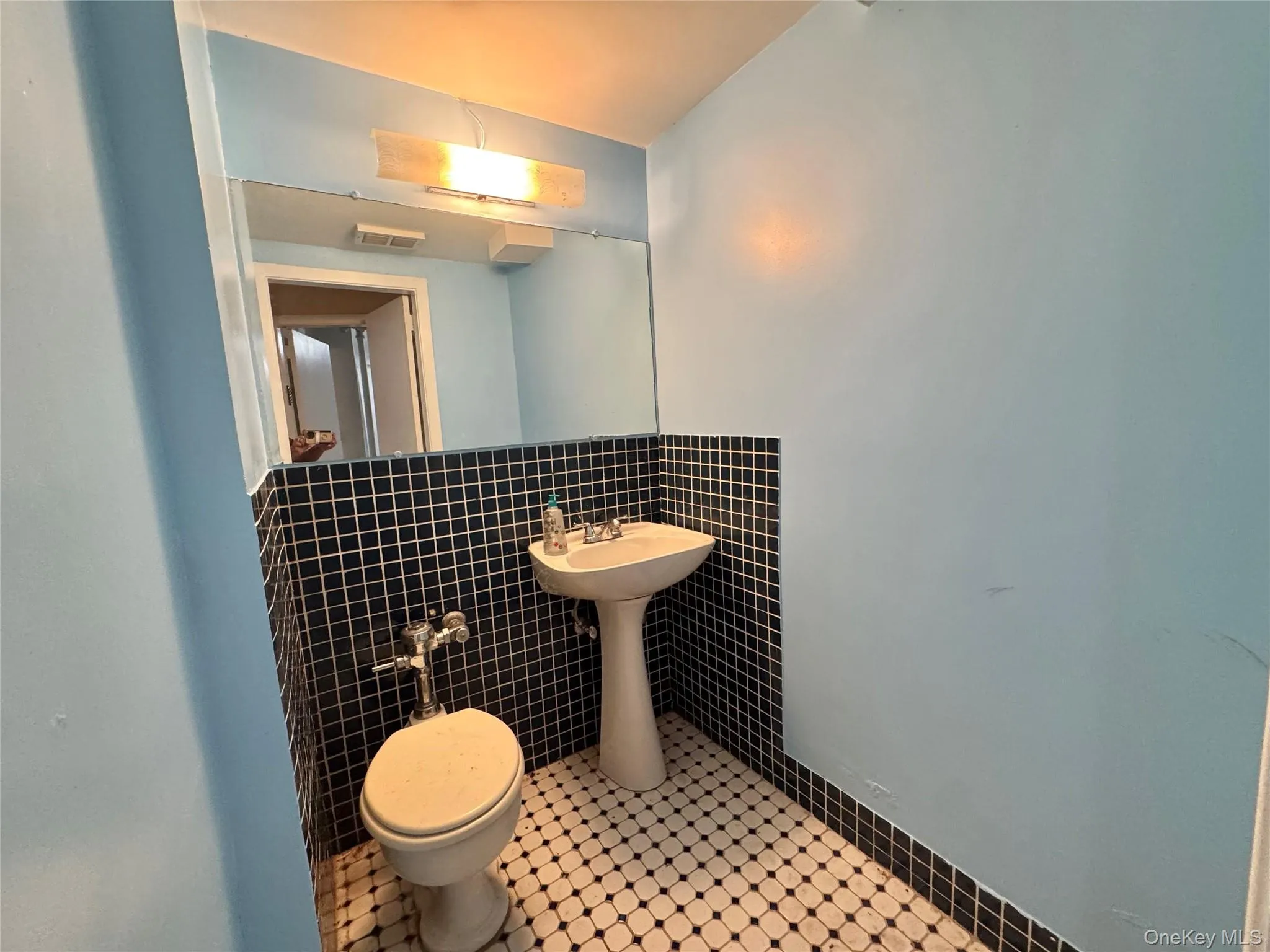 Pedestal sink, wall-mounted mirror, black square tile wainscoting, light blue painted walls, and black and white mosaic tile flooring Pedestal sink, wall-mounted mirror, black square tile wainscoting, light blue painted walls, and black and white mosaic tile flooring