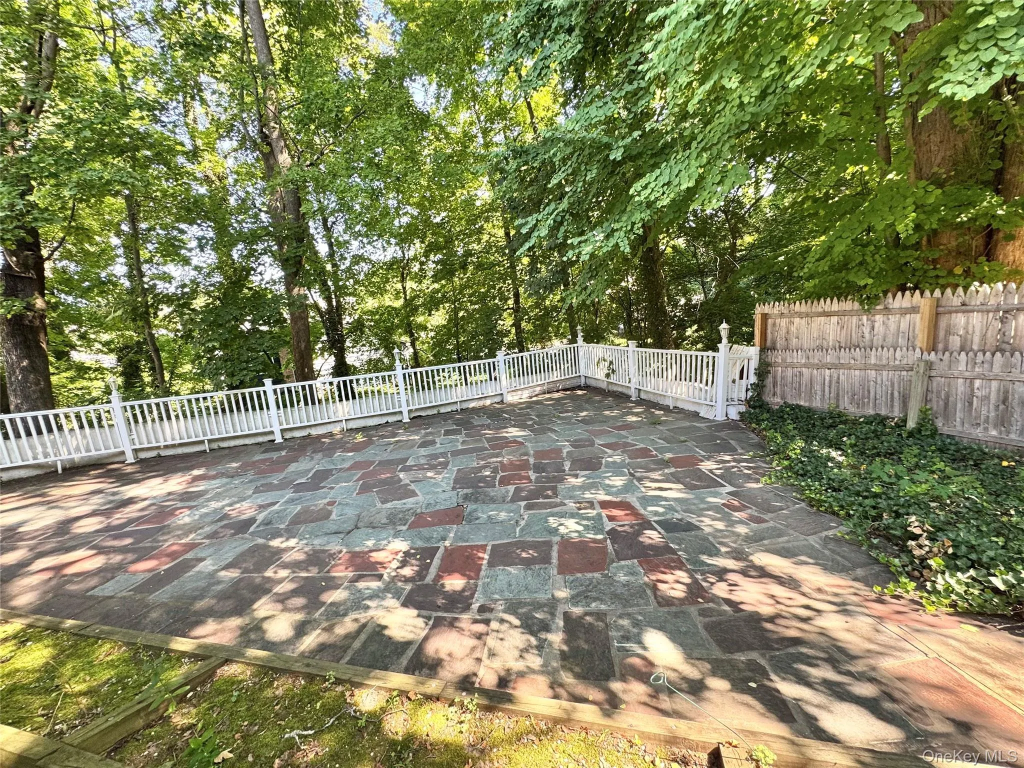 Expansive flagstone patio with a white picket fence, surrounded by mature trees and natural landscaping Expansive flagstone patio with a white picket fence, surrounded by mature trees and natural landscaping