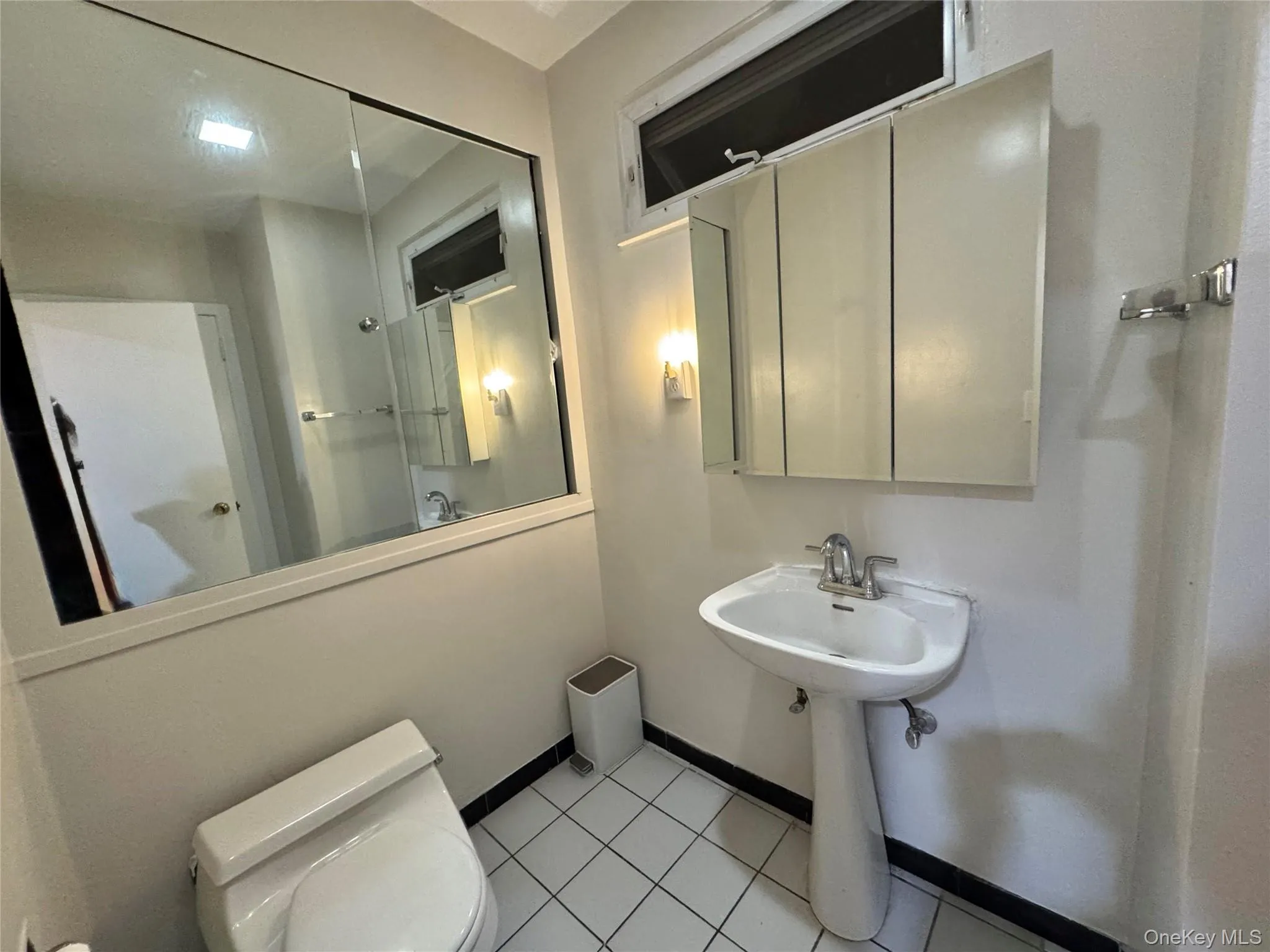 Pedestal sink with chrome faucet, wall-mounted mirrored medicine cabinet, integrated wall mirror, tile flooring, and a transom window Pedestal sink with chrome faucet, wall-mounted mirrored medicine cabinet, integrated wall mirror, tile flooring, and a transom window