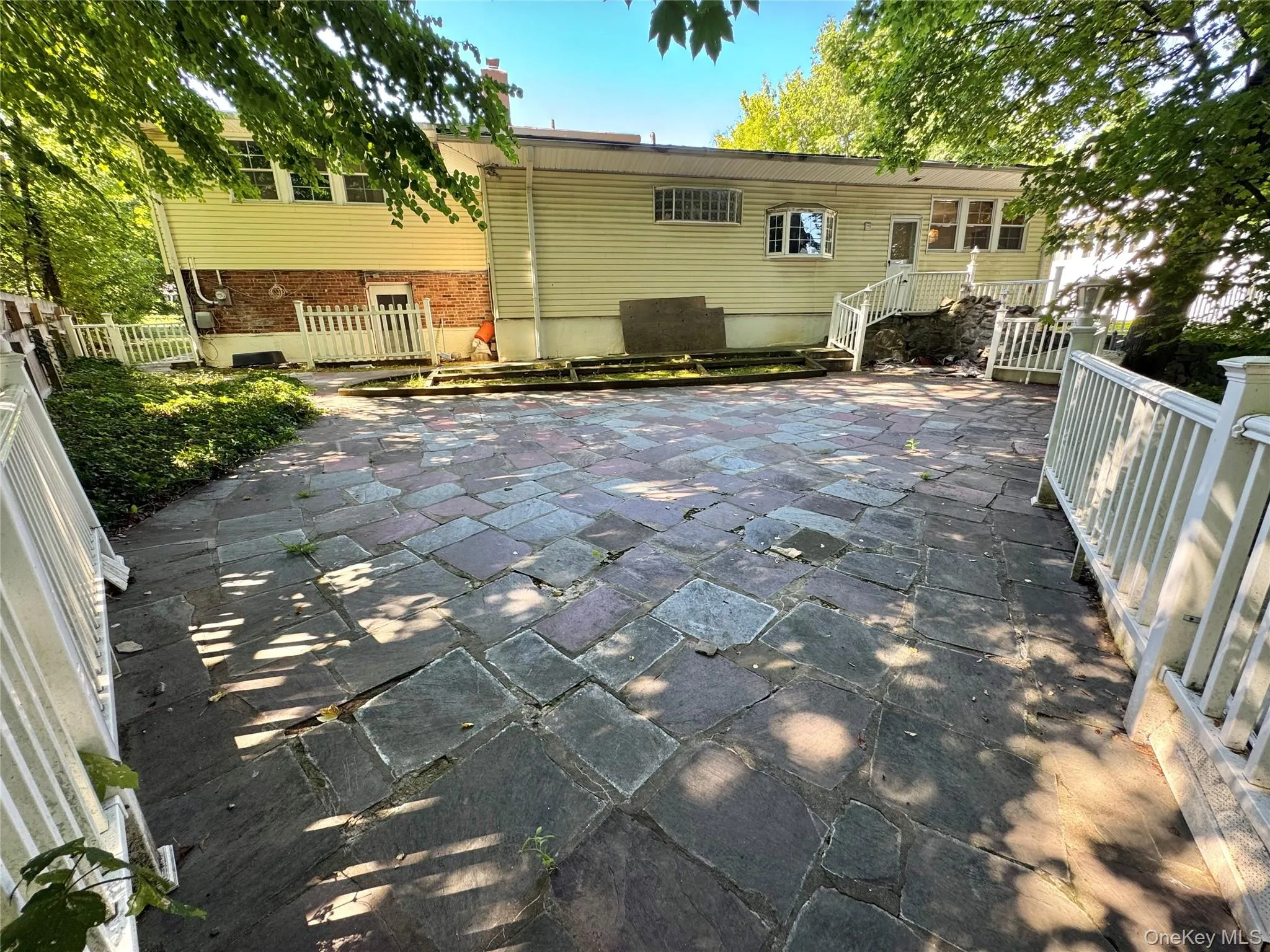 Expansive stone patio with white picket railings and established perimeter plantings Expansive stone patio with white picket railings and established perimeter plantings