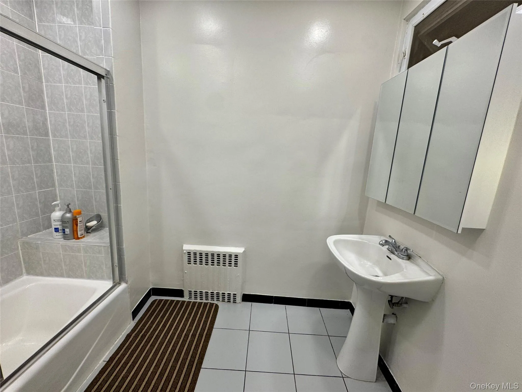 Tub/shower combination with sliding glass enclosure, pedestal sink, wall-mounted mirrored medicine cabinet, and tile flooring Tub/shower combination with sliding glass enclosure, pedestal sink, wall-mounted mirrored medicine cabinet, and tile flooring