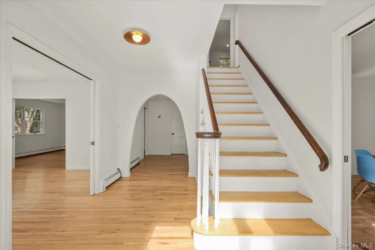 Hardwood flooring, painted white walls, an arched entryway, and a staircase with a wood handrail Hardwood flooring, painted white walls, an arched entryway, and a staircase with a wood handrail