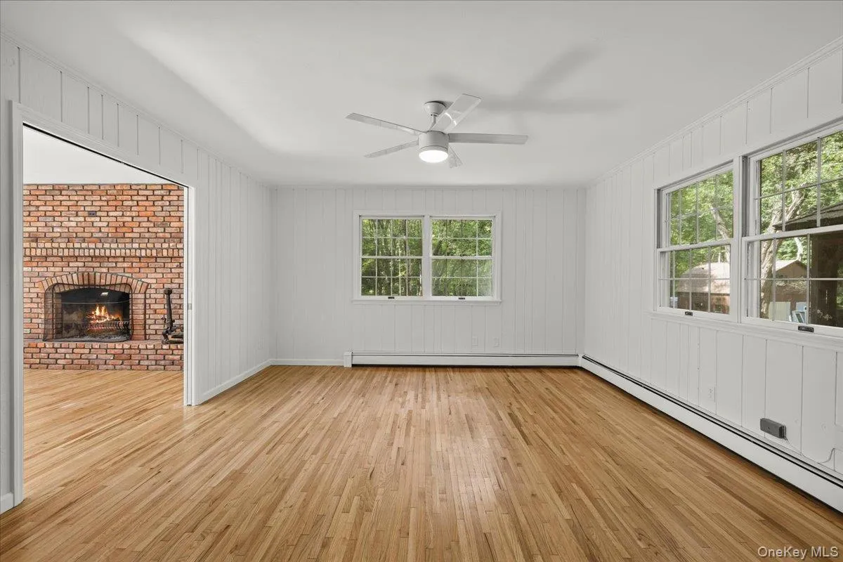 Hardwood flooring, vertical paneling, ceiling fan with integrated lighting, multiple windows, and a brick fireplace Hardwood flooring, vertical paneling, ceiling fan with integrated lighting, multiple windows, and a brick fireplace