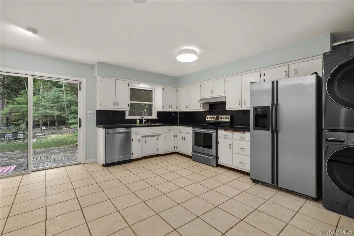Kitchen featuring white cabinetry, black countertops, stainless steel appliances, and tile flooring Kitchen featuring white cabinetry, black countertops, stainless steel appliances, and tile flooring