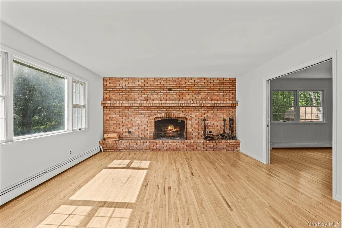 Hardwood flooring, brick-faced fireplace, white walls, and a large window Hardwood flooring, brick-faced fireplace, white walls, and a large window