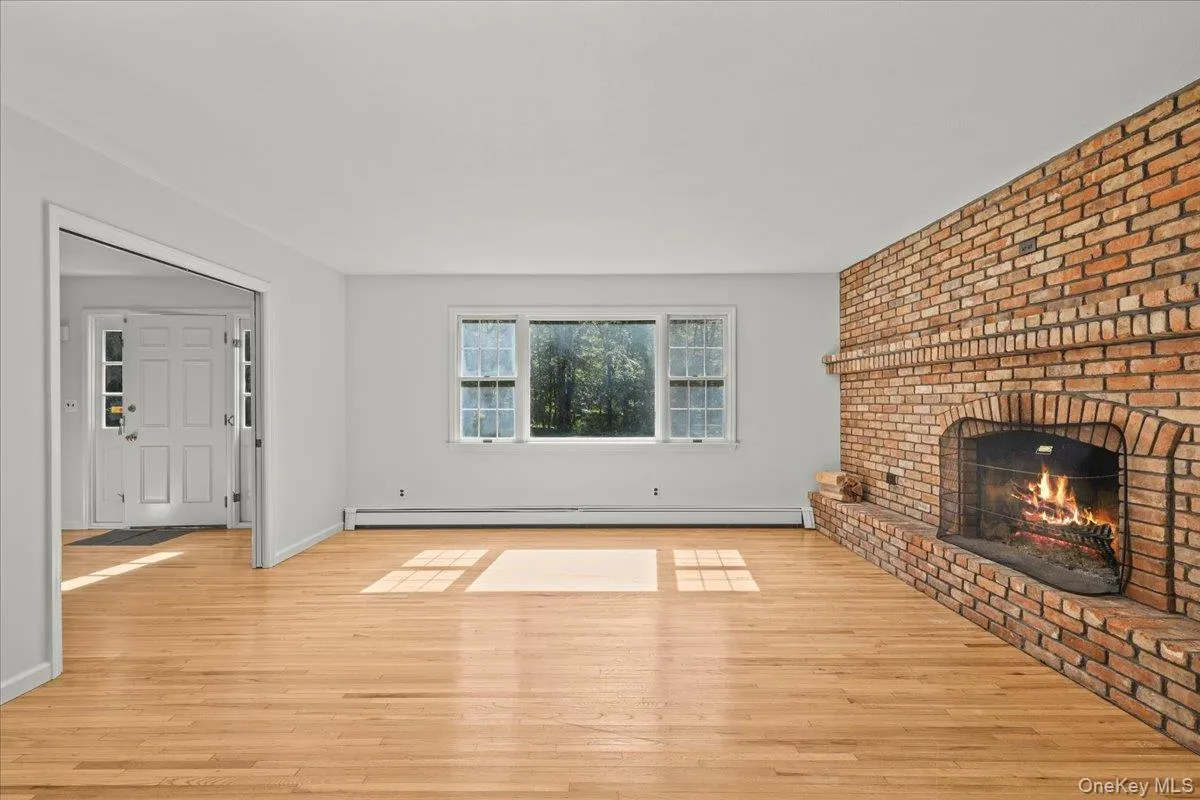 Hardwood flooring, brick fireplace with arched opening, white double-pane windows, and a paneled front door Hardwood flooring, brick fireplace with arched opening, white double-pane windows, and a paneled front door