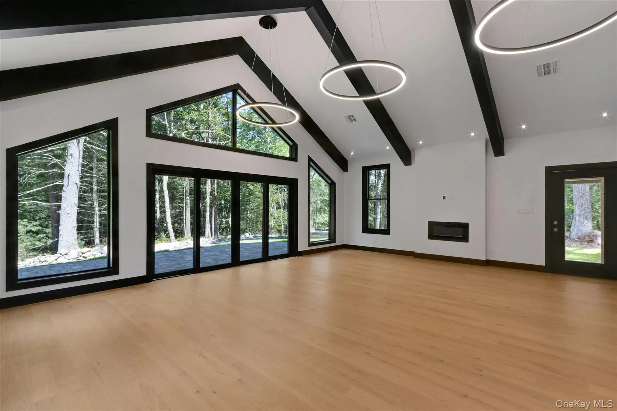 Vaulted ceiling with exposed beams, wood-finish flooring, recessed lighting, linear electric fireplace, and a wall of glass doors Vaulted ceiling with exposed beams, wood-finish flooring, recessed lighting, linear electric fireplace, and a wall of glass doors