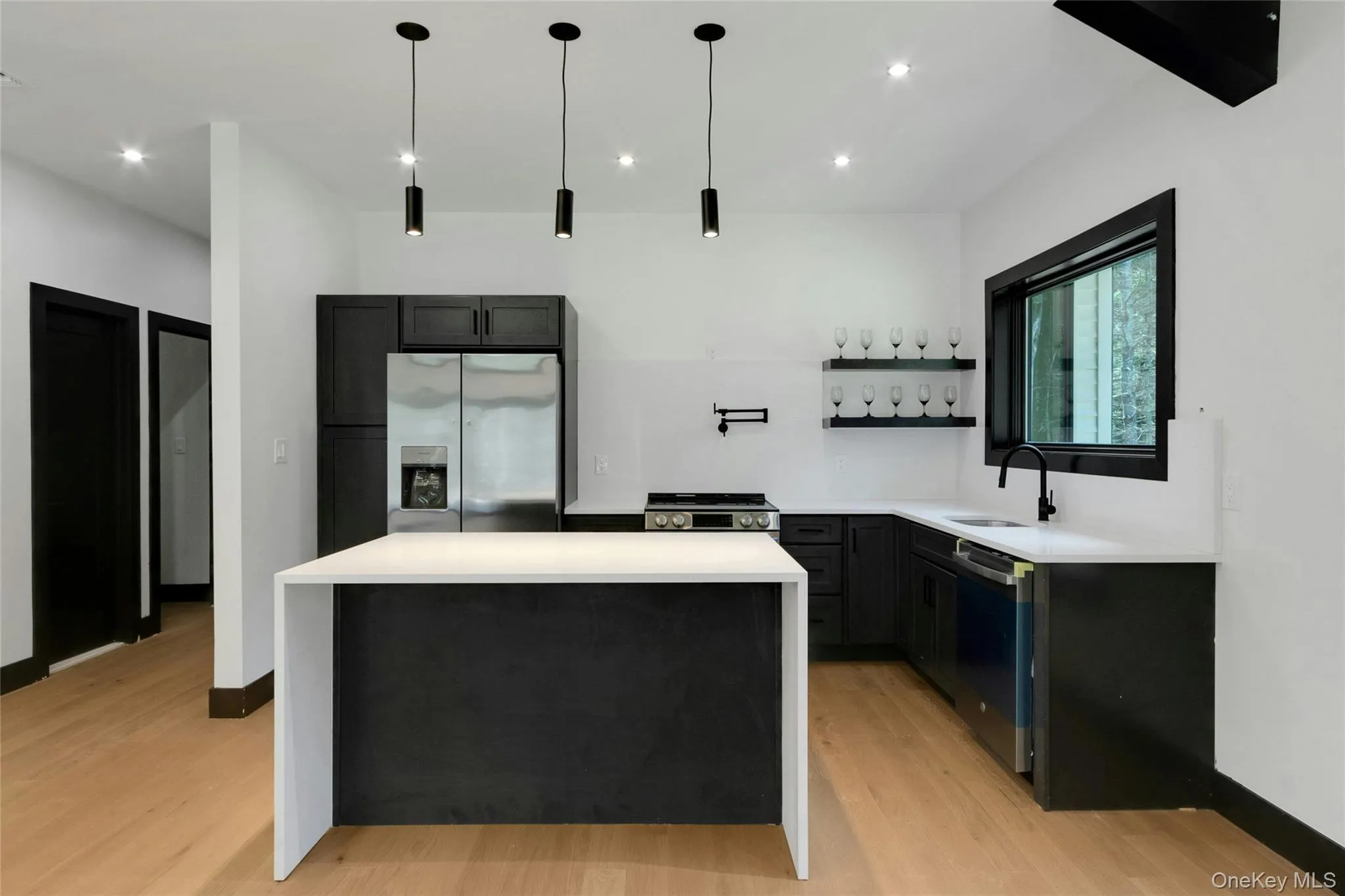 Modern kitchen featuring light wood-finish flooring, dark cabinetry, and white countertops Modern kitchen featuring light wood-finish flooring, dark cabinetry, and white countertops