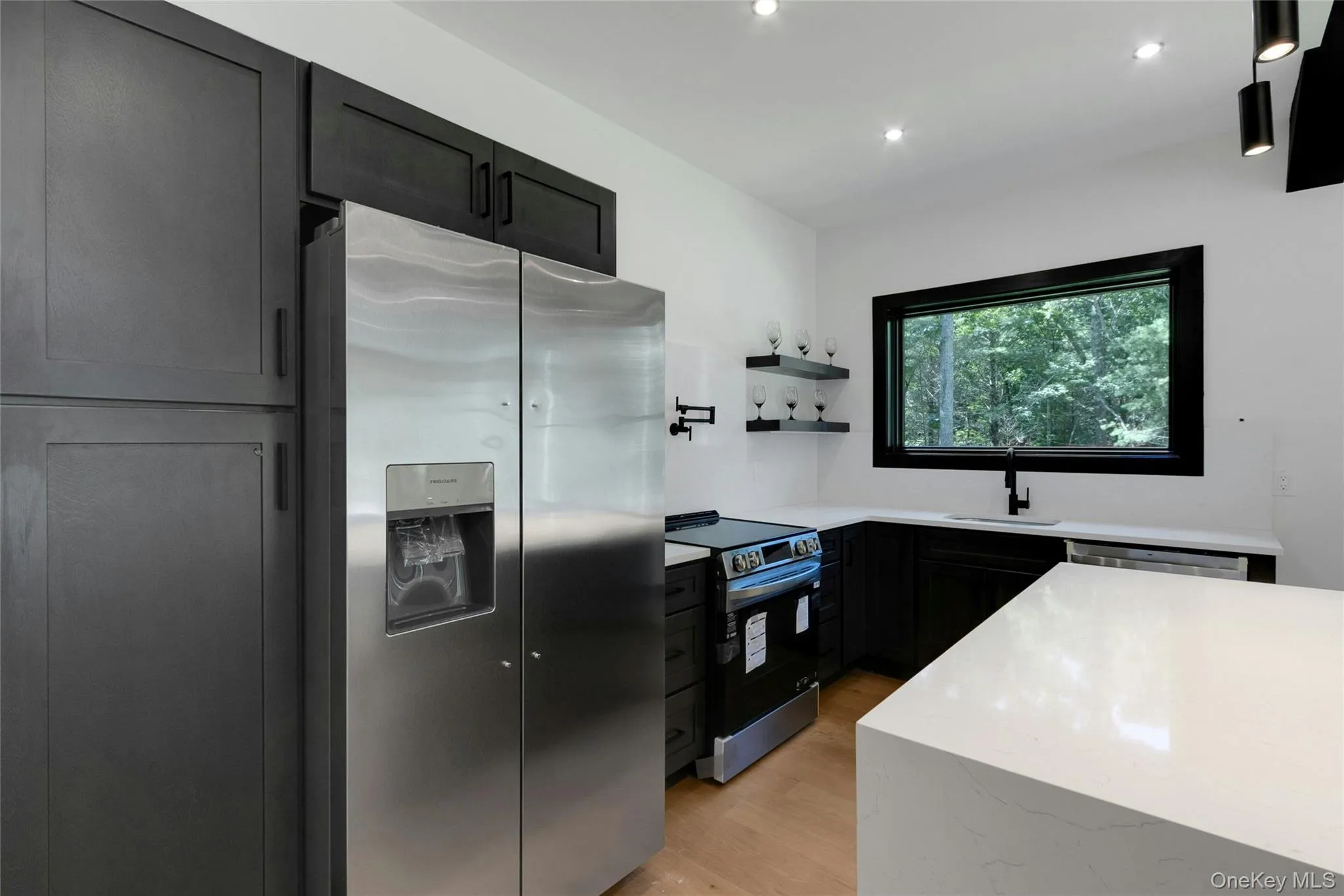 Modern kitchen featuring dark cabinetry, stainless steel appliances, light countertops, and wood-finish flooring Modern kitchen featuring dark cabinetry, stainless steel appliances, light countertops, and wood-finish flooring