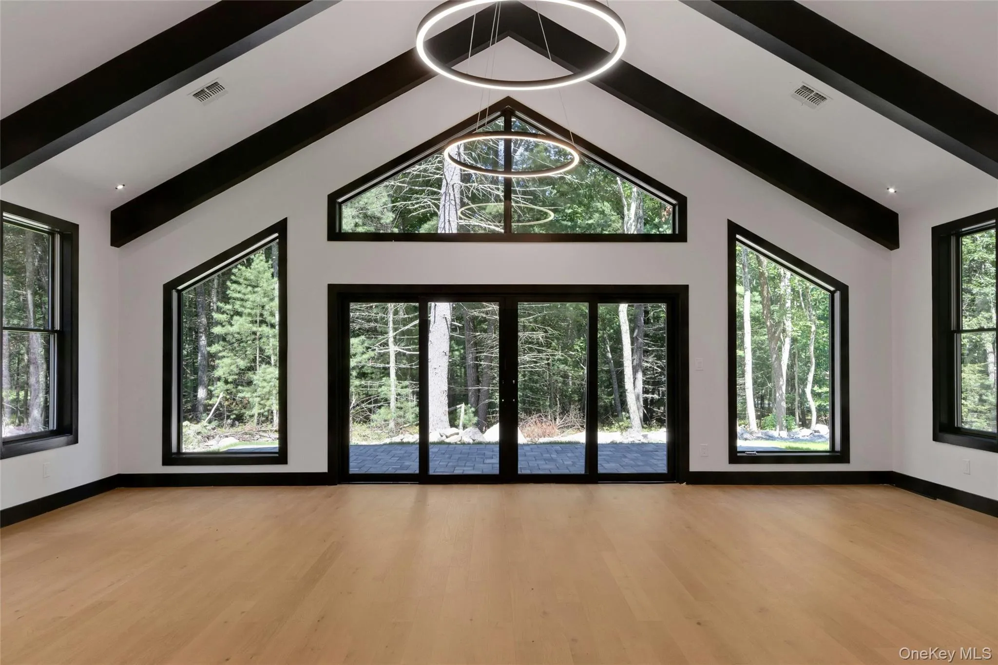 Vaulted ceiling with exposed black beams, light wood-finish flooring, recessed lighting, and large windows with black frames Vaulted ceiling with exposed black beams, light wood-finish flooring, recessed lighting, and large windows with black frames