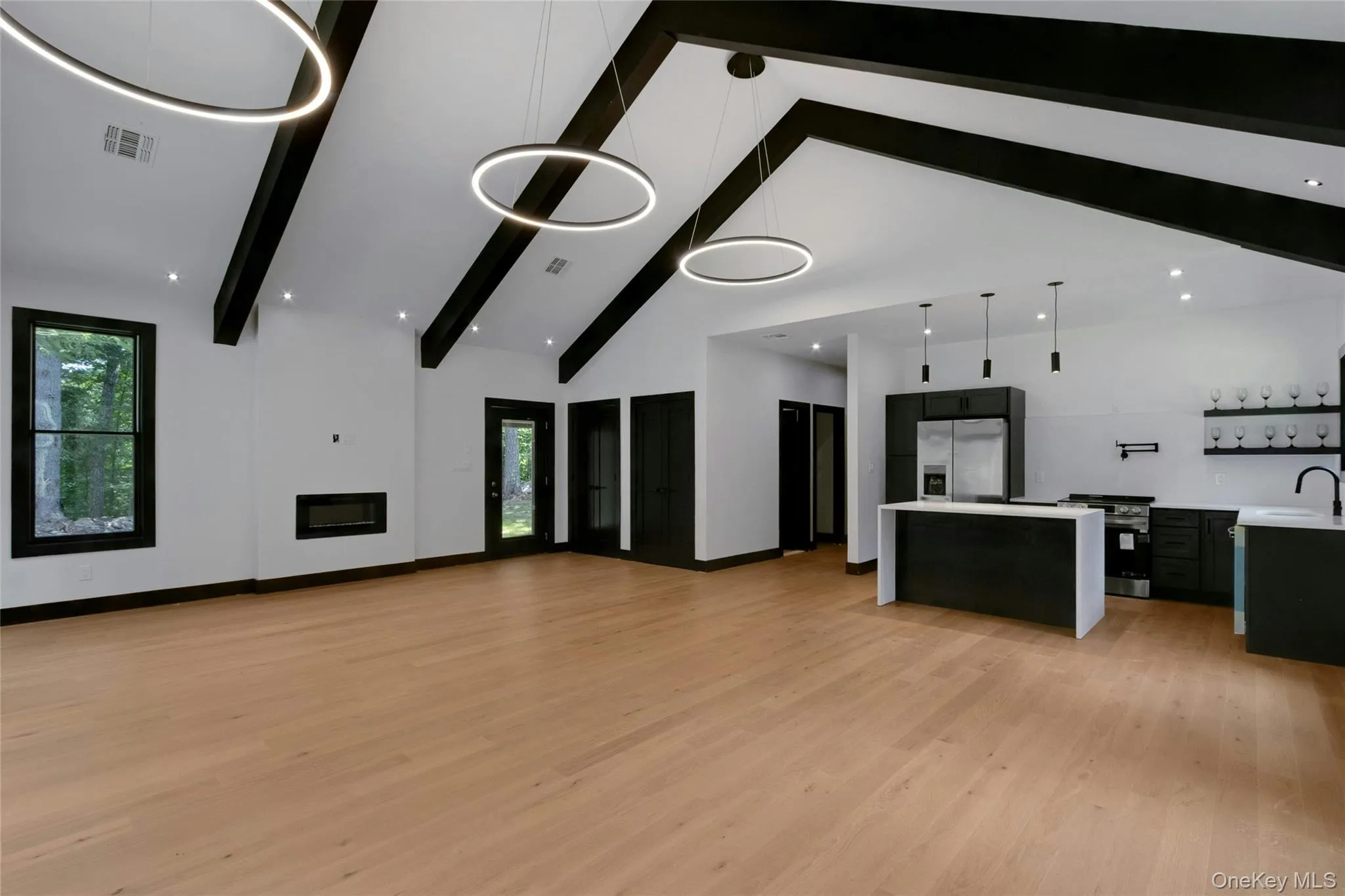 Vaulted ceiling with exposed beams, wood-finish flooring, linear electric fireplace, kitchen island with counter seating, and modern pendant lighting Vaulted ceiling with exposed beams, wood-finish flooring, linear electric fireplace, kitchen island with counter seating, and modern pendant lighting
