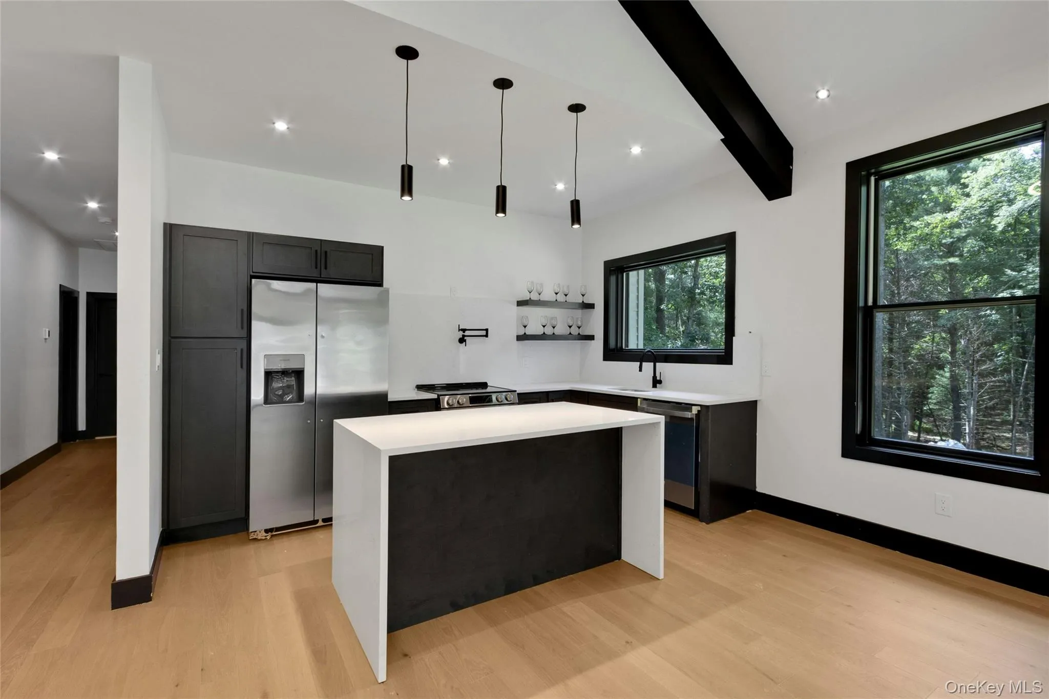 Contemporary kitchen featuring dark cabinetry, stainless steel appliances, a center island with a white countertop, and wood-finish flooring Contemporary kitchen featuring dark cabinetry, stainless steel appliances, a center island with a white countertop, and wood-finish flooring