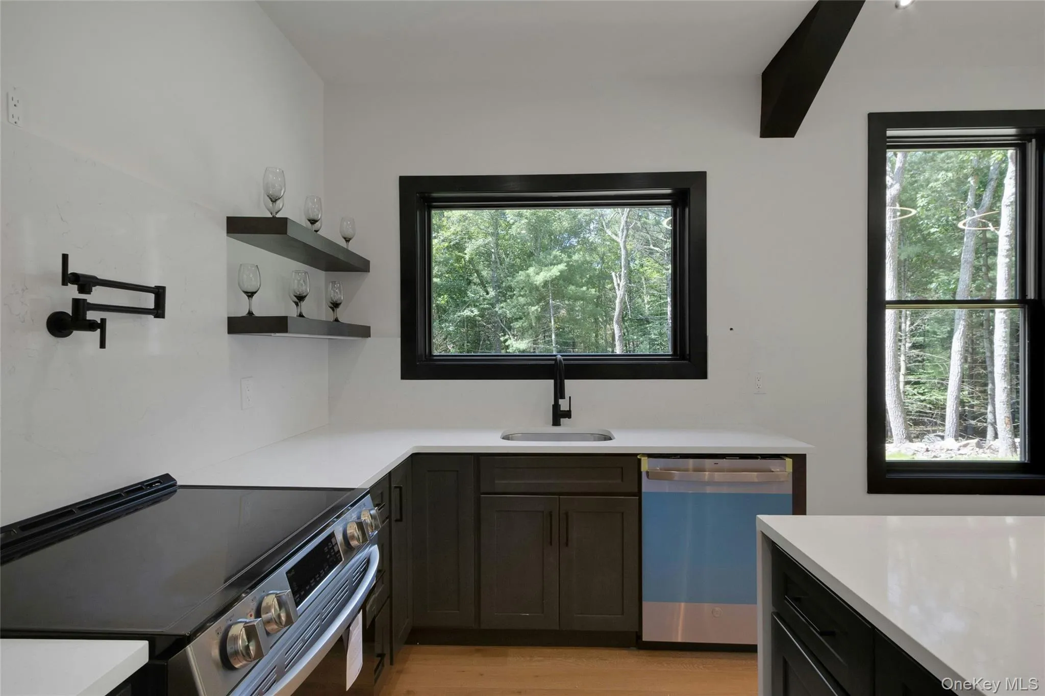 White countertops, dark wood-finish cabinetry, black-framed windows, built-in wall shelves, and a black pot filler White countertops, dark wood-finish cabinetry, black-framed windows, built-in wall shelves, and a black pot filler