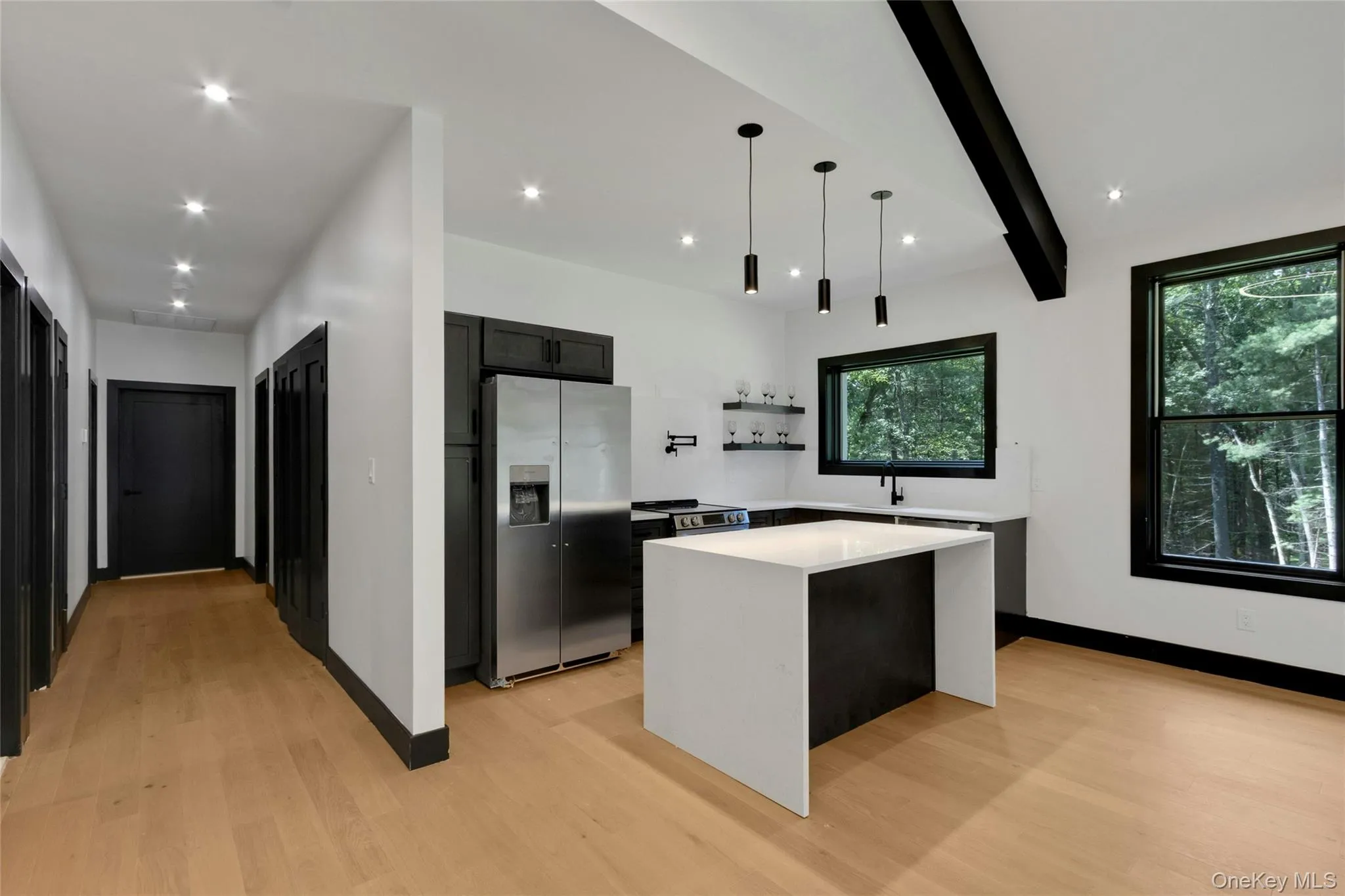 Open-concept kitchen with a waterfall island, pendant lighting, stainless steel appliances, and wood-finish flooring Open-concept kitchen with a waterfall island, pendant lighting, stainless steel appliances, and wood-finish flooring