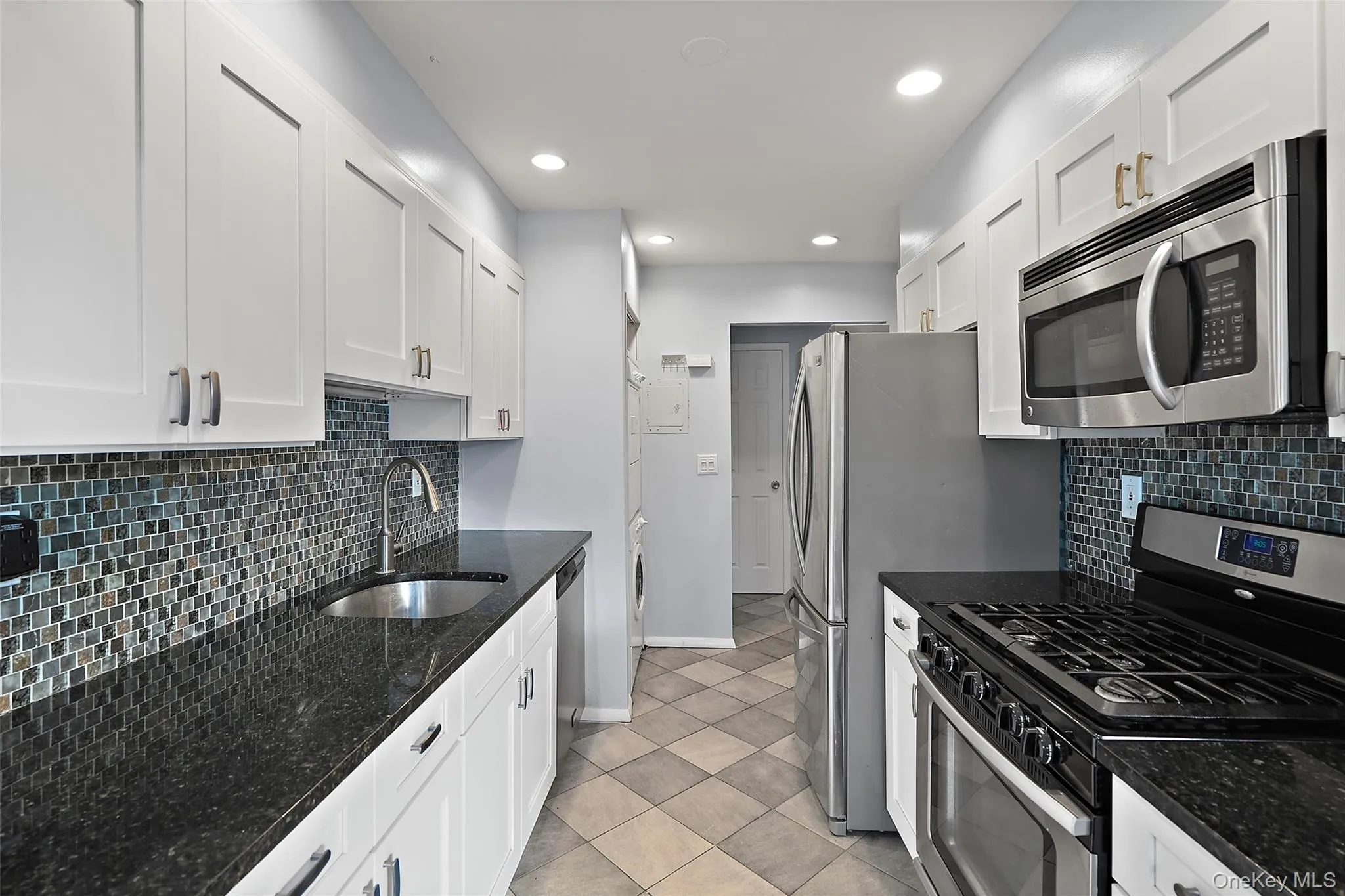 Kitchen with tasteful backsplash, stainless steel appliances, sink, dark stone countertops, and white cabinets Kitchen with tasteful backsplash, stainless steel appliances, sink, dark stone countertops, and white cabinets