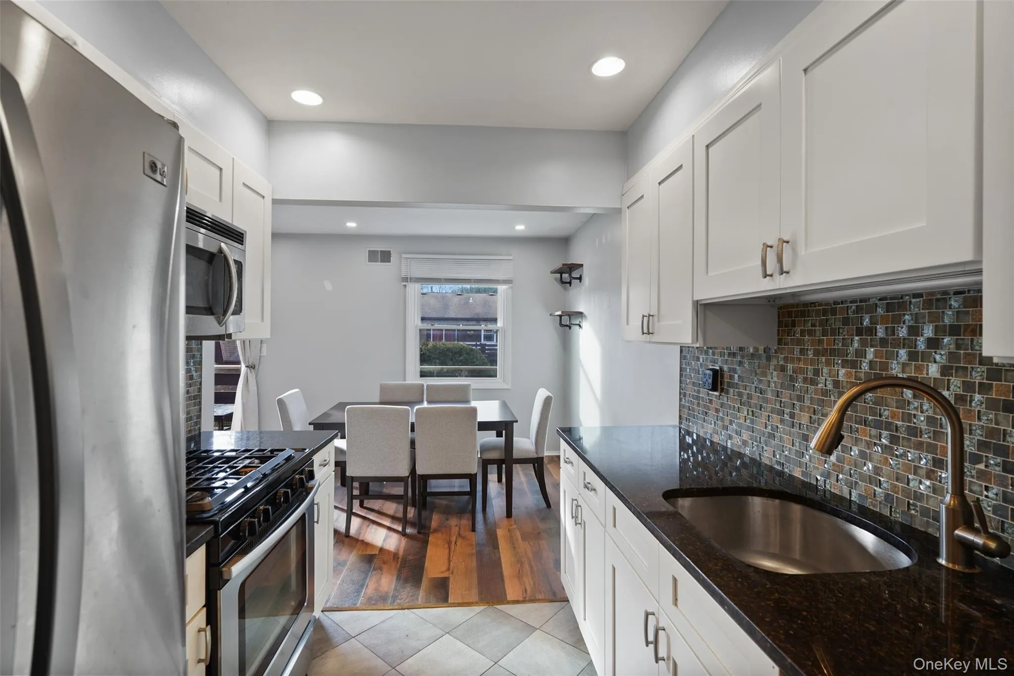 Kitchen featuring sink, light hardwood / wood-style flooring, dark stone countertops, appliances with stainless steel finishes, and white cabinetry Kitchen featuring sink, light hardwood / wood-style flooring, dark stone countertops, appliances with stainless steel finishes, and white cabinetry