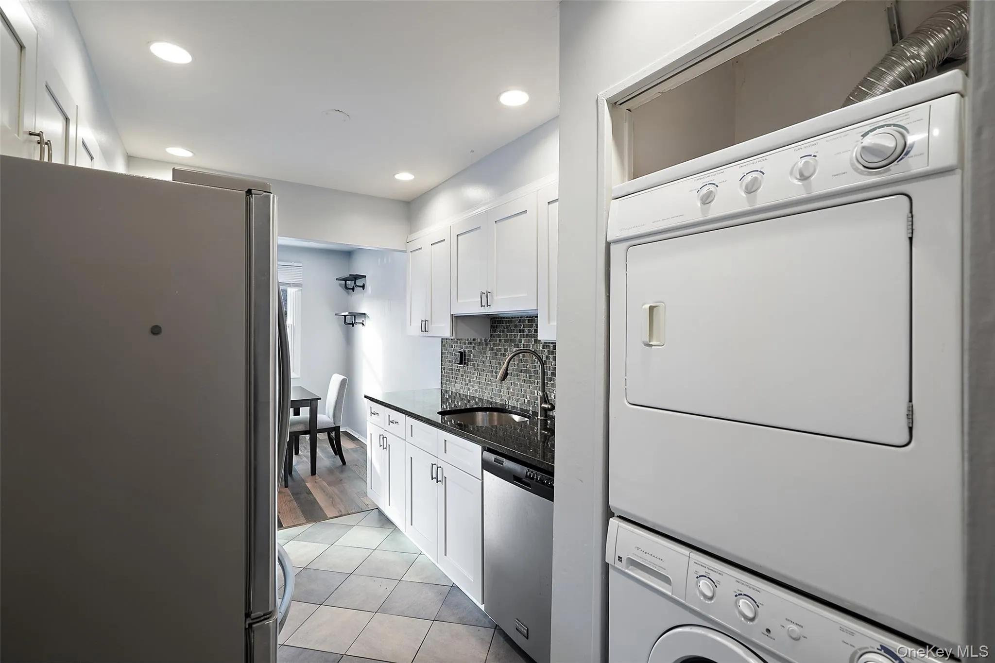 Kitchen featuring appliances with stainless steel finishes, sink, light tile patterned floors, stacked washer and clothes dryer, and white cabinetry Kitchen featuring appliances with stainless steel finishes, sink, light tile patterned floors, stacked washer and clothes dryer, and white cabinetry