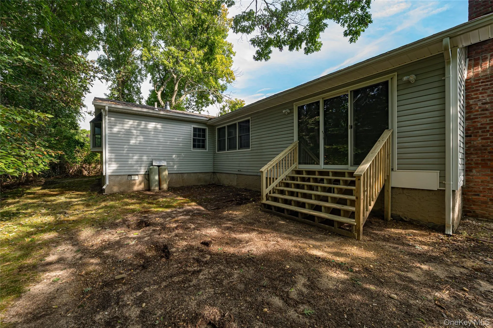 Spacious single-story home featuring a new wooden staircase and multiple access points, surrounded by mature landscaping and a generous yard with natural shade from established trees Spacious single-story home featuring a new wooden staircase and multiple access points, surrounded by mature landscaping and a generous yard with natural shade from established trees