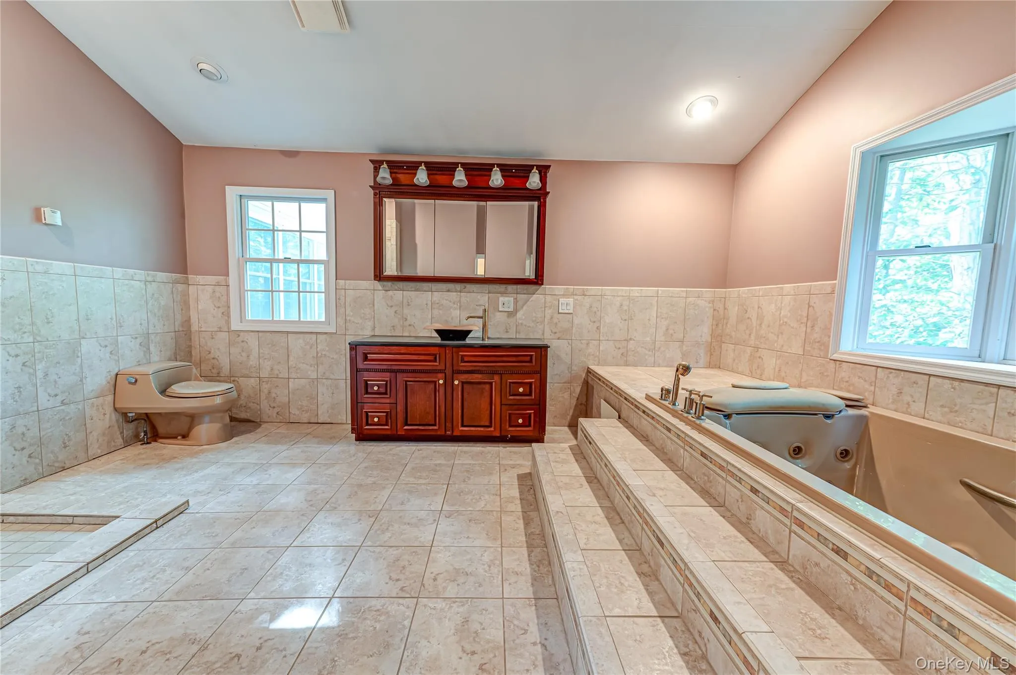 Built-in bathtub with steps and tiled surround, tiled flooring, wood-finish vanity with vessel sink, and recessed lighting Built-in bathtub with steps and tiled surround, tiled flooring, wood-finish vanity with vessel sink, and recessed lighting
