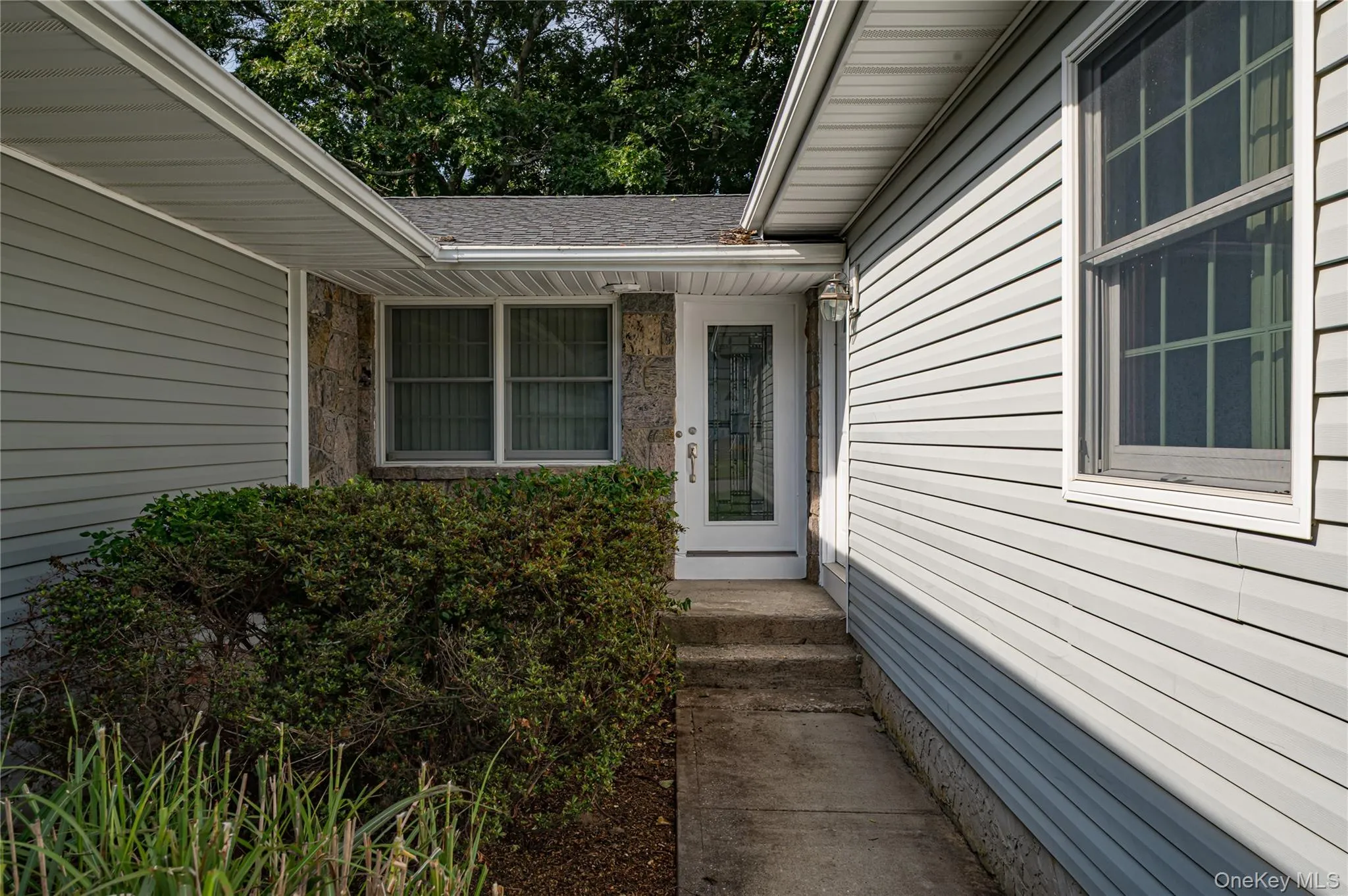 Exterior featuring light-toned siding, stone accents, and a white entry door with decorative glass Exterior featuring light-toned siding, stone accents, and a white entry door with decorative glass