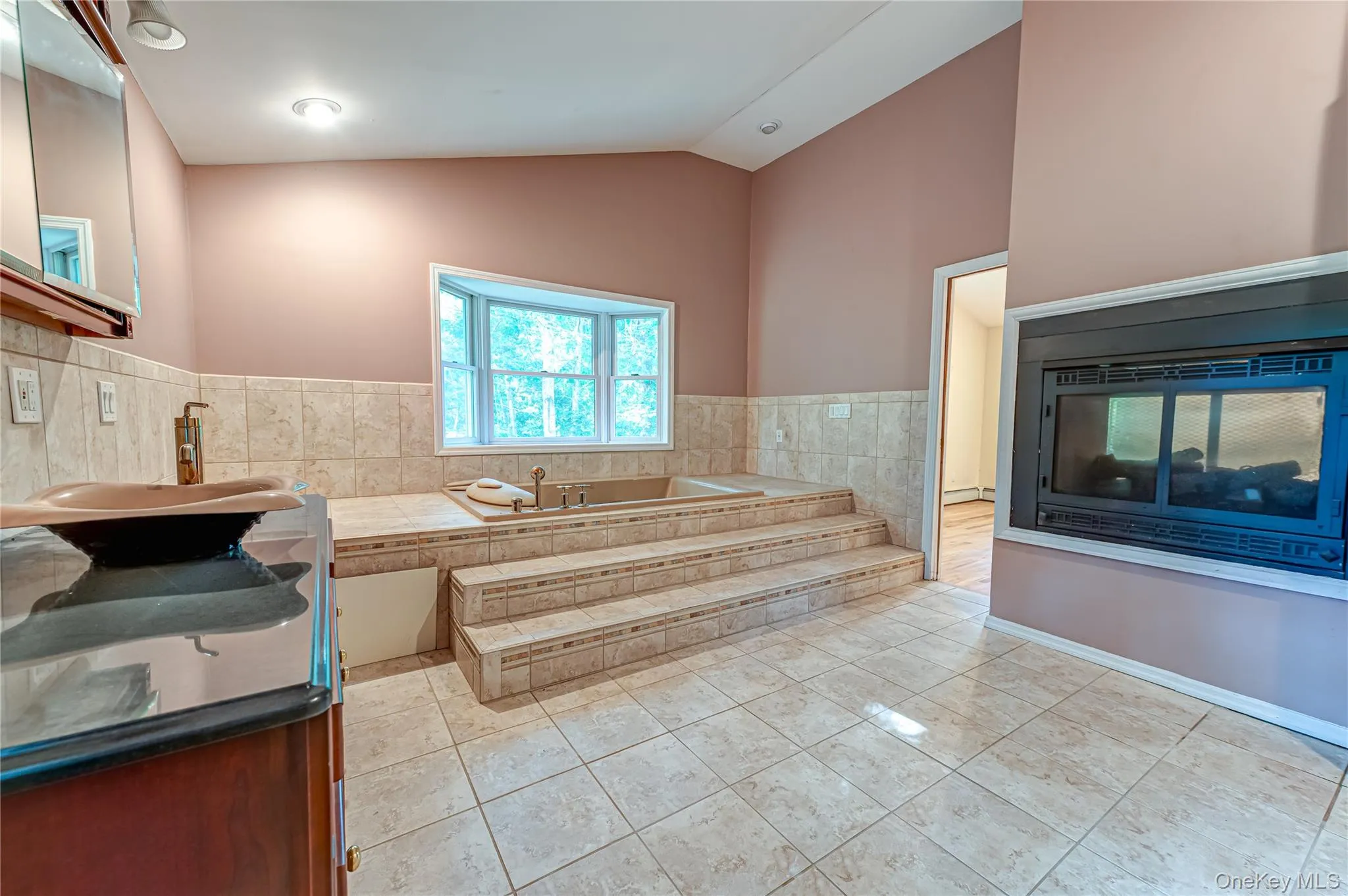 Tile flooring, double sided fireplace, elevated built-in tub, bay window, and vanity with vessel sink Tile flooring, double sided fireplace, elevated built-in tub, bay window, and vanity with vessel sink