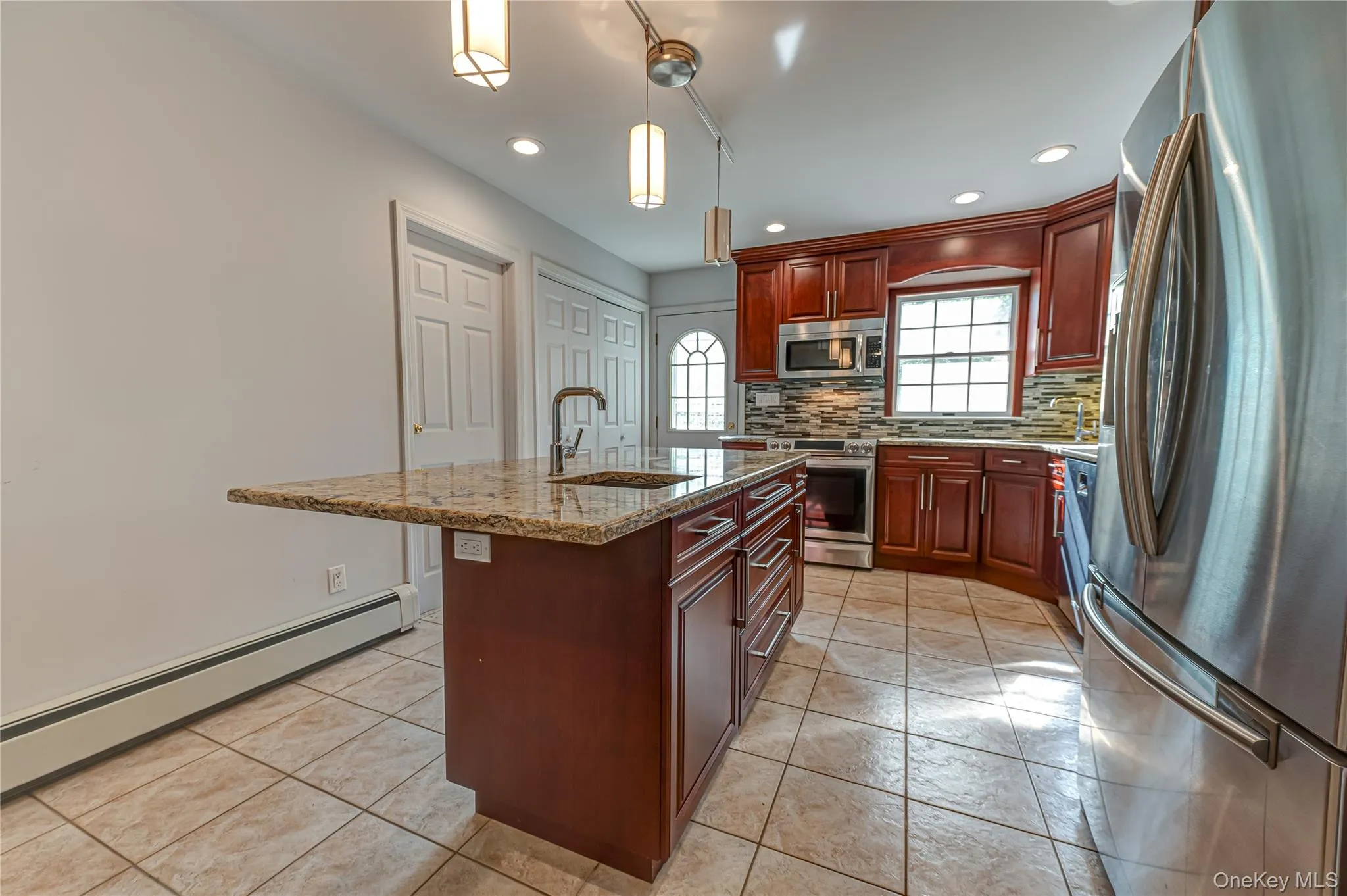 Kitchen featuring a central island with granite countertop, wood cabinetry, stainless steel appliances, and tile flooring Kitchen featuring a central island with granite countertop, wood cabinetry, stainless steel appliances, and tile flooring