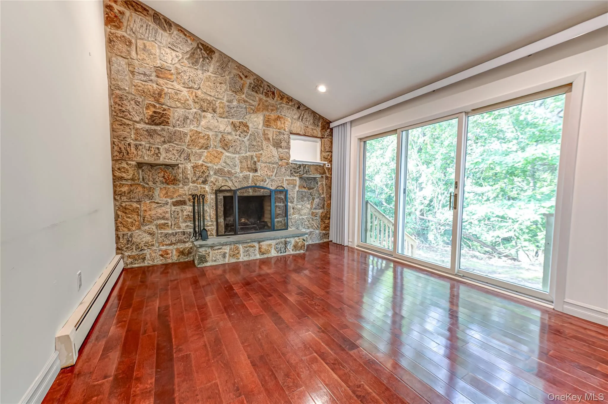 Vaulted ceiling, stone-clad fireplace with hearth, recessed lighting, wood-finish flooring, and sliding glass doors Vaulted ceiling, stone-clad fireplace with hearth, recessed lighting, wood-finish flooring, and sliding glass doors