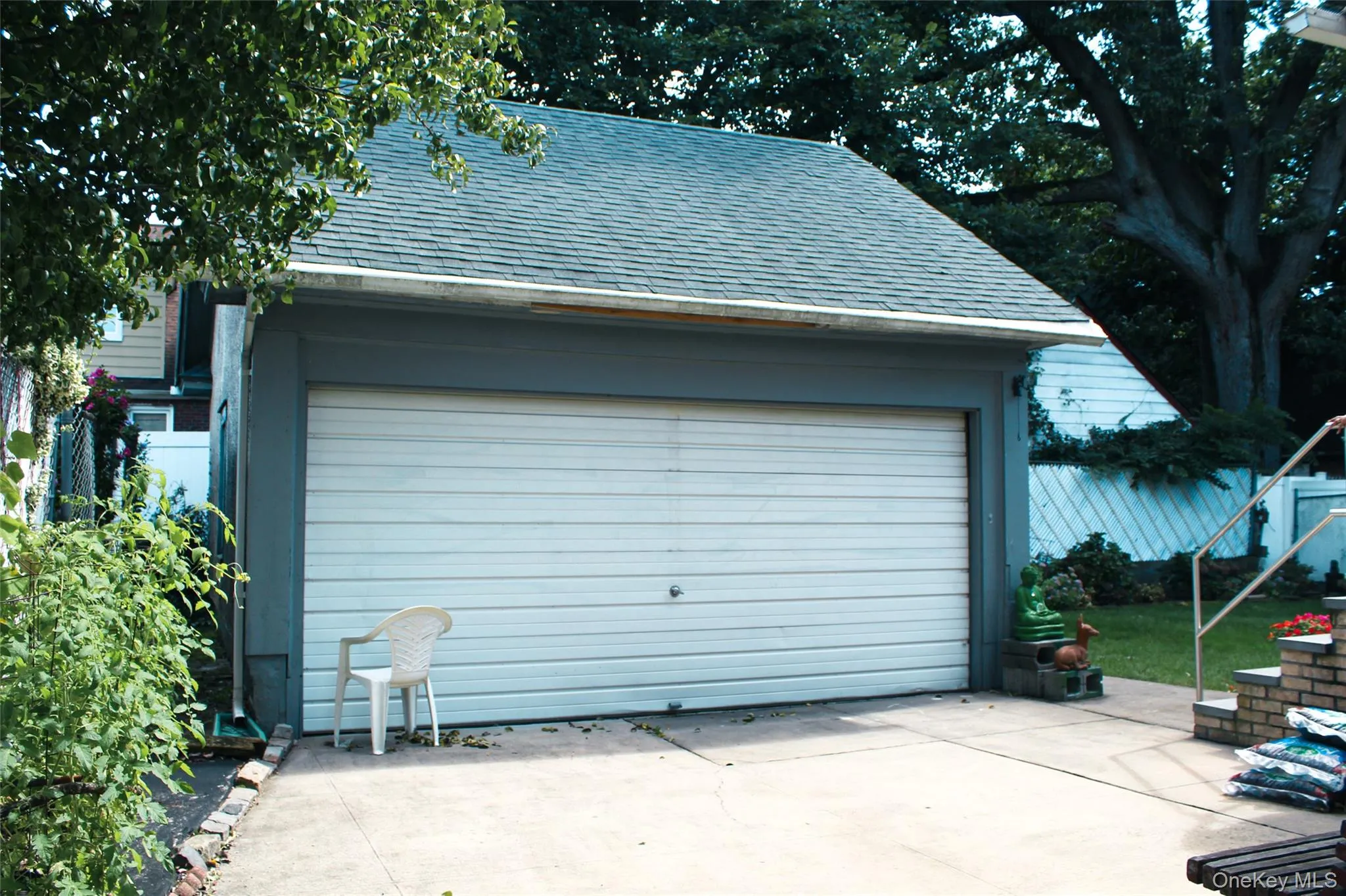 Detached remote opening garage with a double vehicle door, asphalt shingle roof, and concrete driveway Detached remote opening garage with a double vehicle door, asphalt shingle roof, and concrete driveway